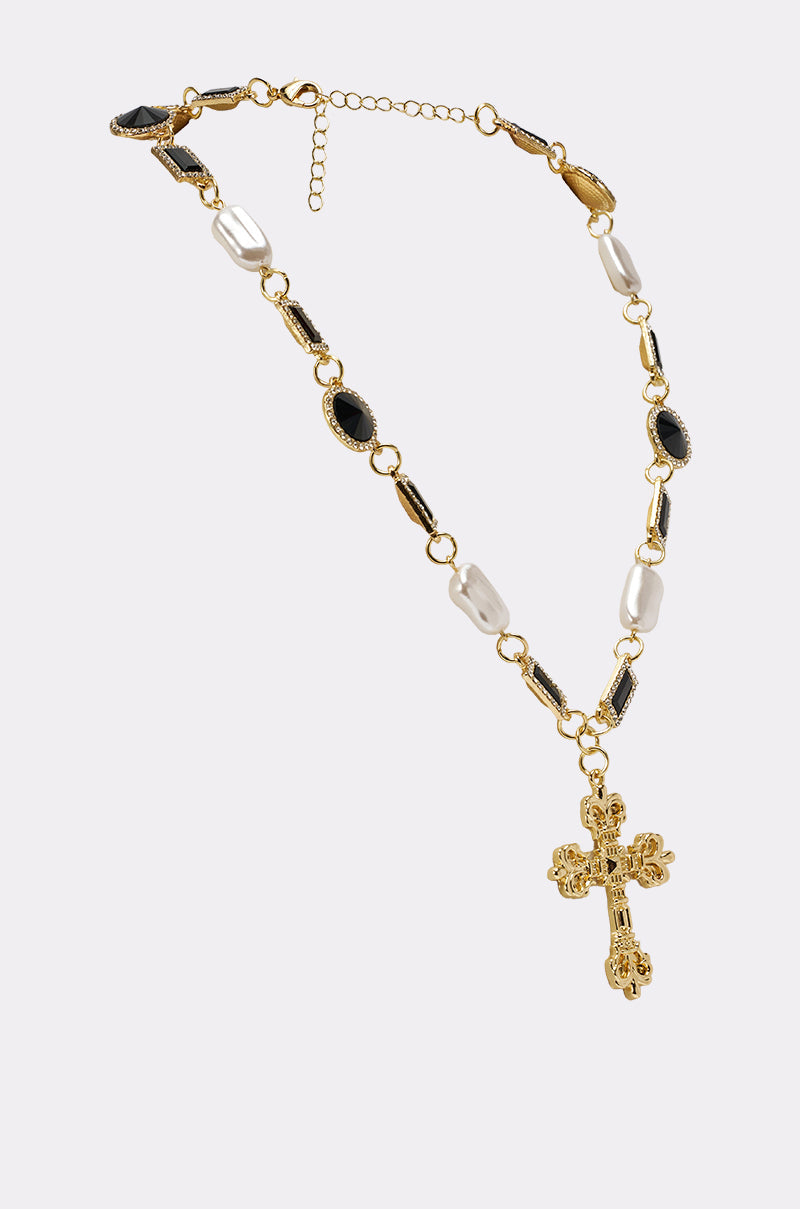 The WITH THE TIMES NECKLACE features a gothic-glam design with a gold-tone chain, black stones, white pearls, and a large ornate gold cross pendant, displayed against a light background. 3