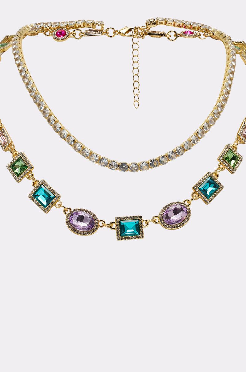 Two gold necklaces—one is a rhinestone necklace with clear round stones, and the RAY NECKLACE features rectangular and oval green, blue, and purple gemstones. Both are displayed against a white background. 3