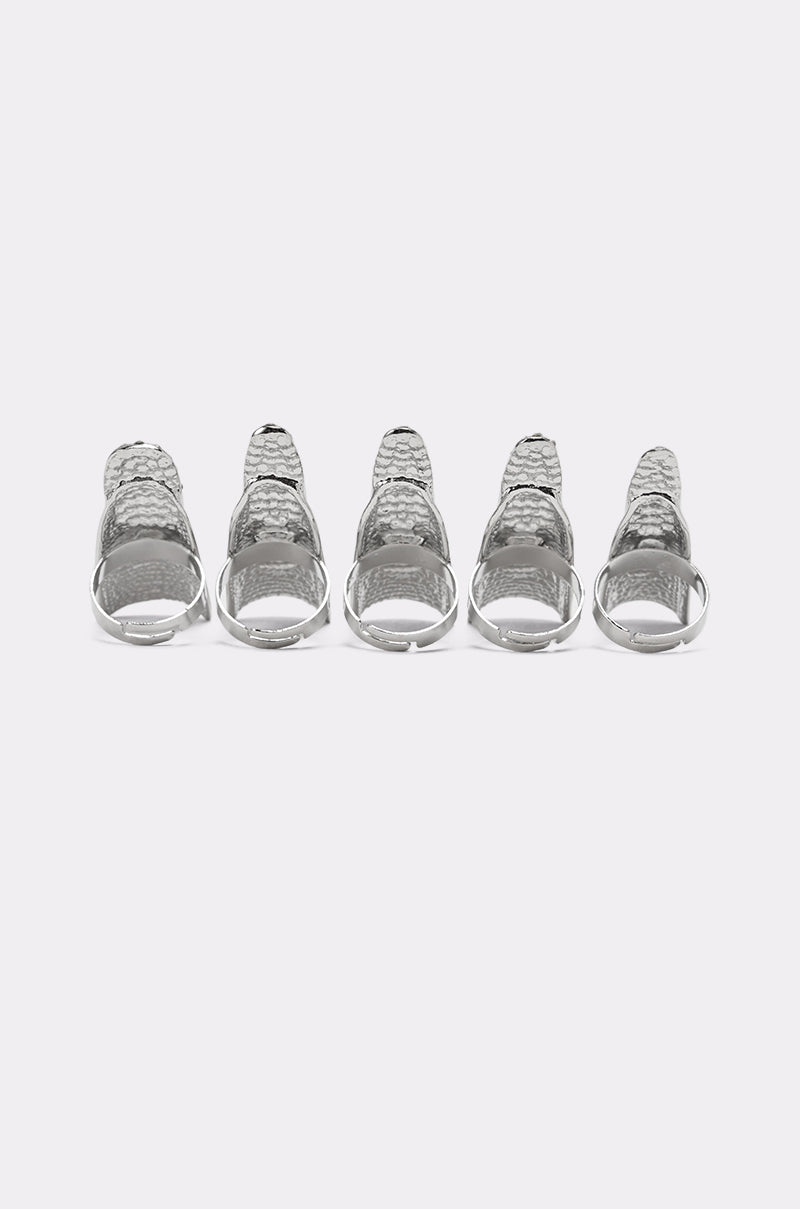 The STELLA RING SET showcases five silver, textured rings—some with rhinestone pavé—standing upright in a row on a plain white background, each evenly spaced for a striking, bold display. 5
