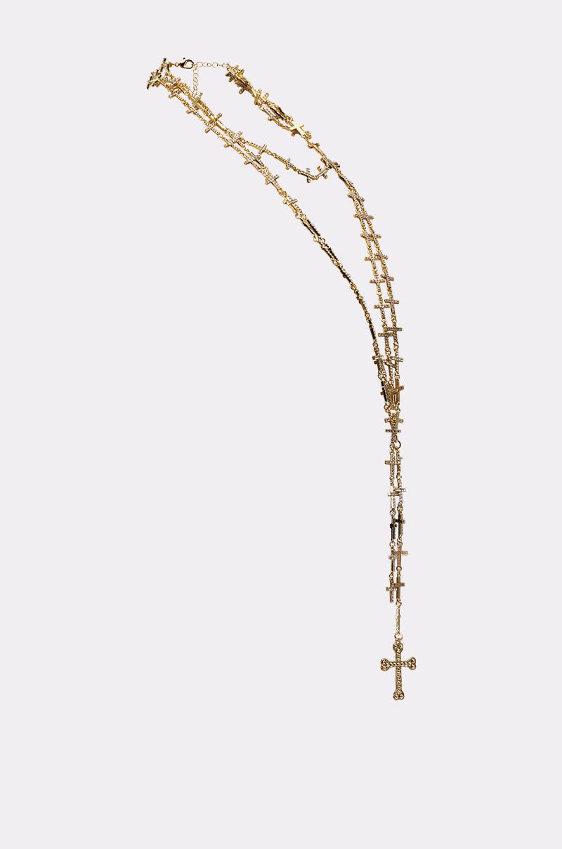 THE ONE NECKLACE is a gold-tone statement piece featuring multiple small crosses along the chain and a larger cross pendant at the end, shown against a plain white background. 3