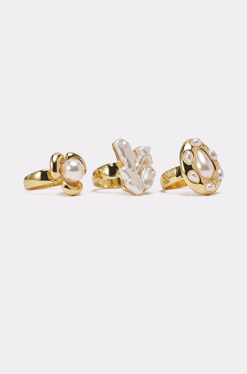 The SUSIE RING SET features three gold rings with unique designs, each adorned with a white pearl. The rings are arranged upright in a row against a plain white background.