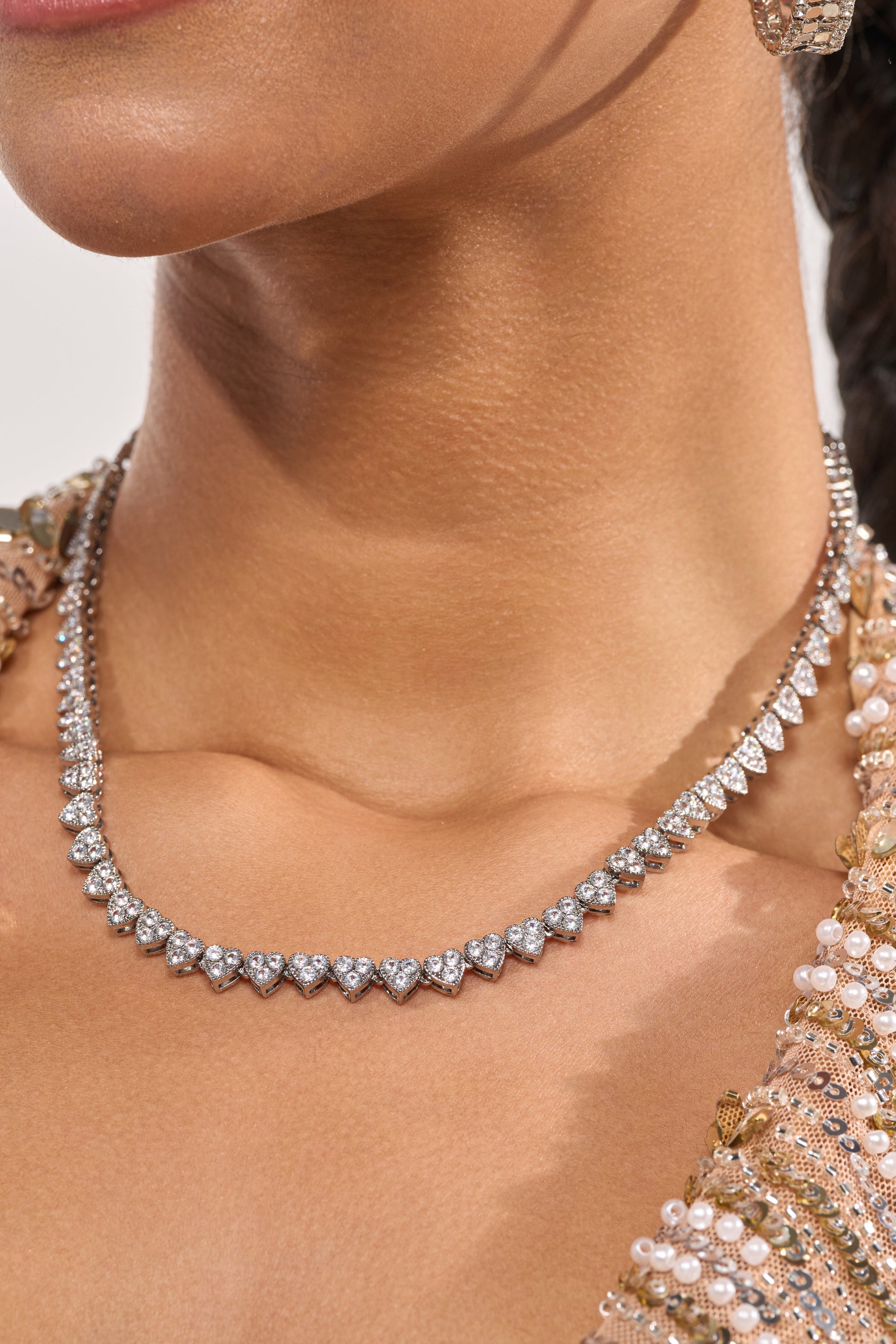 A close-up of a woman’s neck and collarbone adorned with the REALLY LIKE THAT LUXE NECKLACE, featuring sparkling triangular stones. She wears a gold and pearl embroidered garment, her skin glowing with a smooth, warm tone. 1