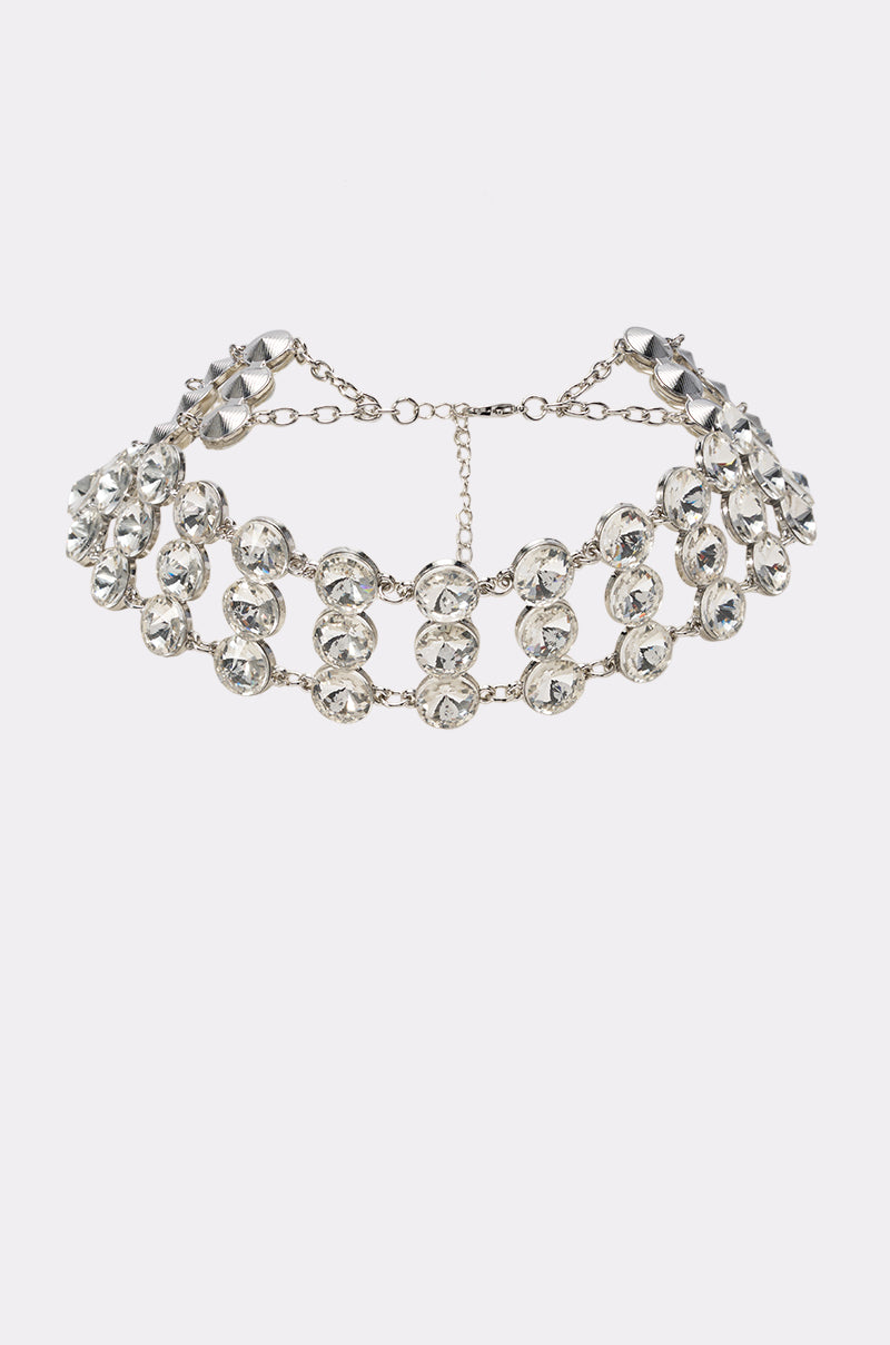 The GLAM LIFE NECKLACE is a dazzling silver-tone choker featuring two rows of large, clear rhinestones and a secure chain clasp at the back, perfect as an elegant eveningwear accessory. It is displayed on a plain white background.