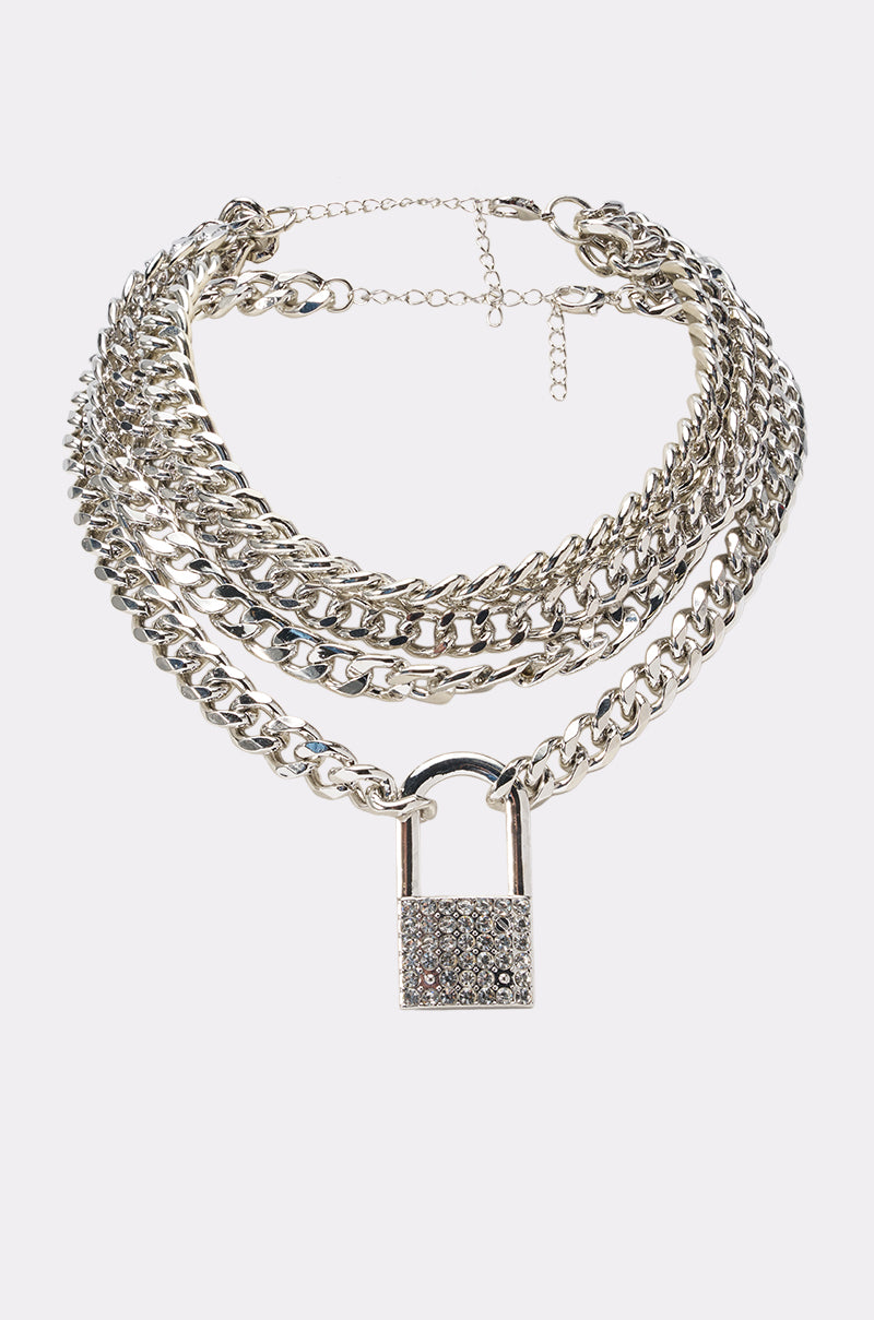 The KEEP IT ON LOCK NECKLACE is a layered silver chain with a bold, sparkling rhinestone lock pendant, shown against a white background. 0