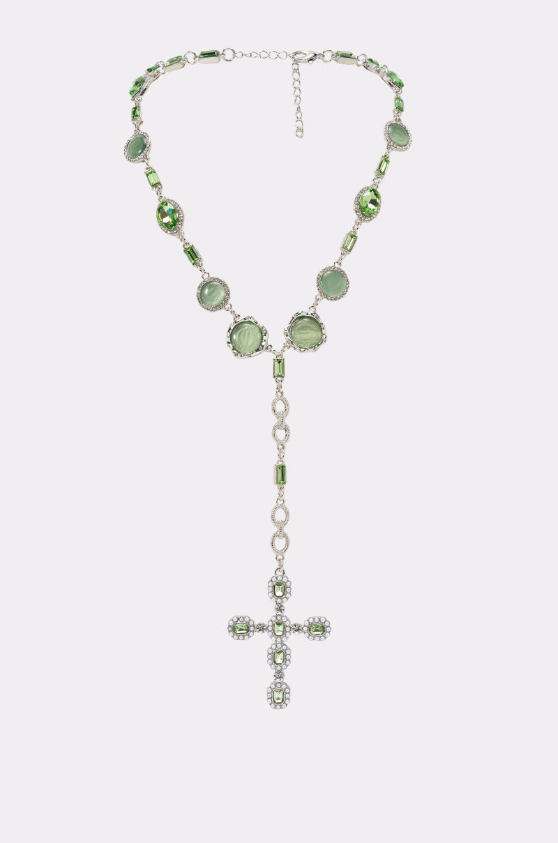 The WHATS THE WORD NECKLACE is a rosary-style lariat featuring green beads, gemstones, and a jeweled silver cross pendant—a bold and vibrant pick for festival jewelry.
