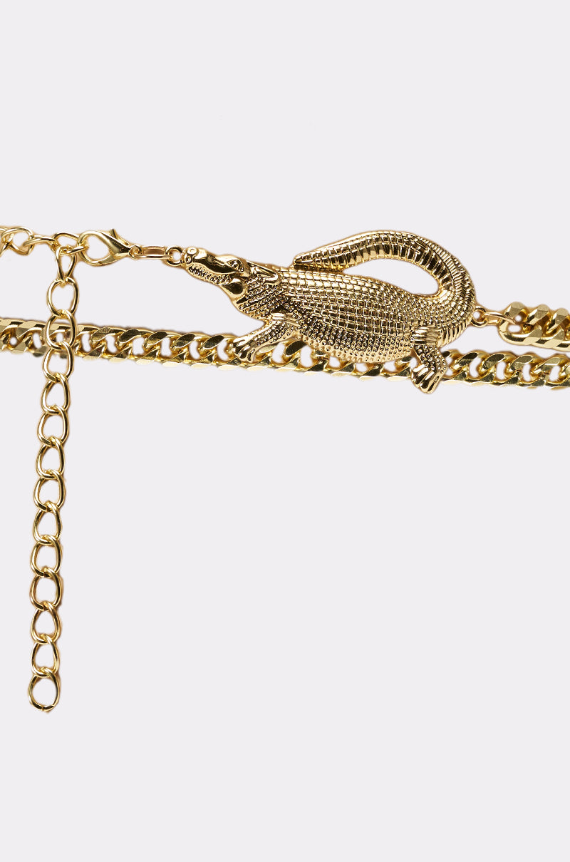 The BITE ME CHAIN BELT is a gold chain accessory with a detailed crocodile buckle clasp, showcased on a plain white background—a bold statement piece. 3