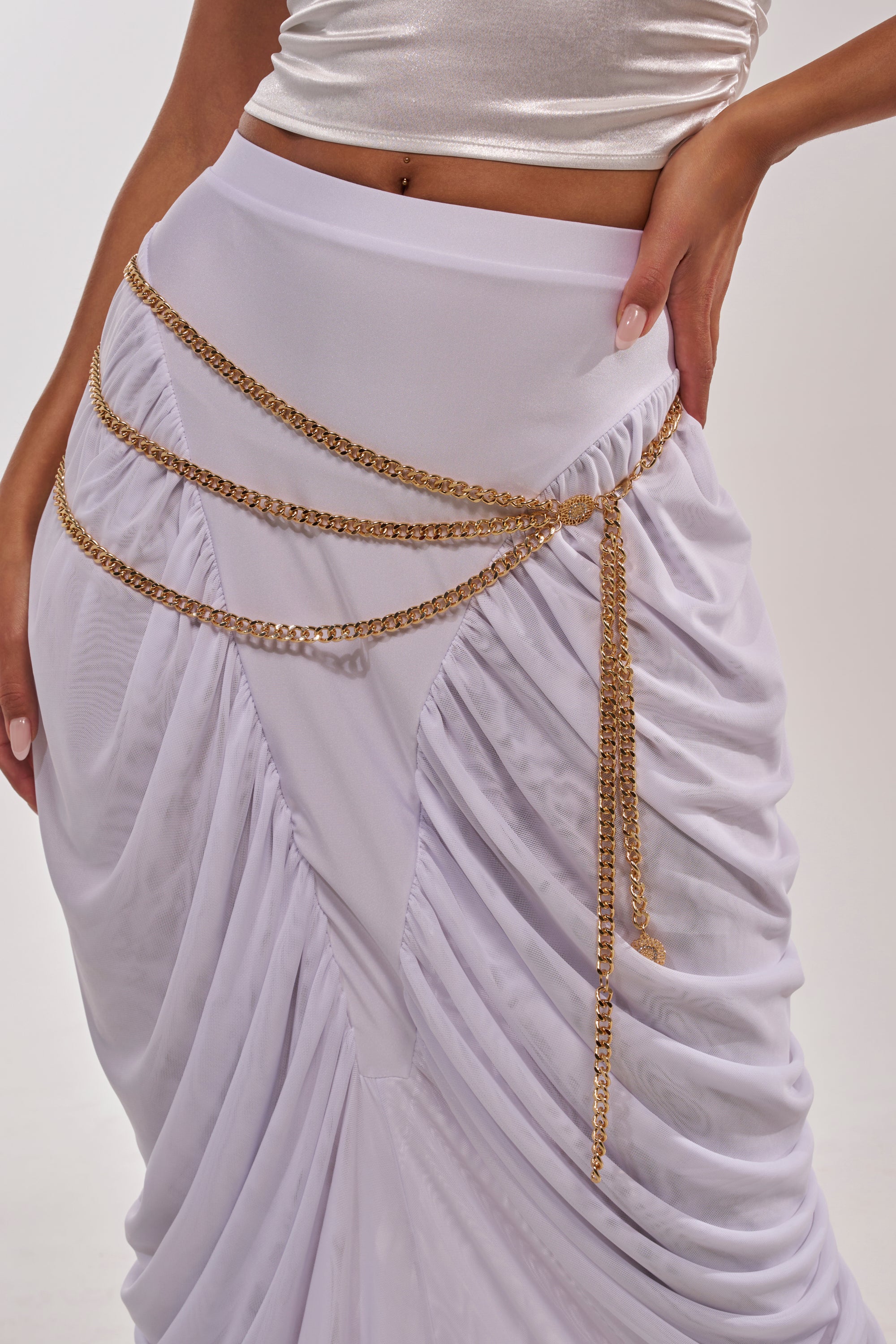 A woman poses with one hand on her hip, wearing a white ruched skirt and a shiny silver crop top, accessorized by the BUY ME DESIGNER CHAIN BELT draped at her hips—making it a true statement piece against a plain background. 0