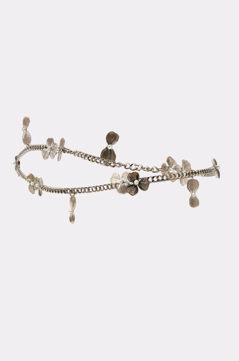 The FLORAL BITS CHAIN BELT is a silver chain belt featuring small, textured flower-shaped charms delicately arranged along its length, shown against a plain white background. 2