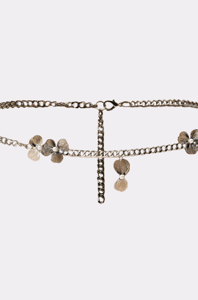 The FLORAL BITS CHAIN BELT is a gold statement waist belt with textured floral accents and a vertical dangling chain at the center, shown on a plain white background. 3