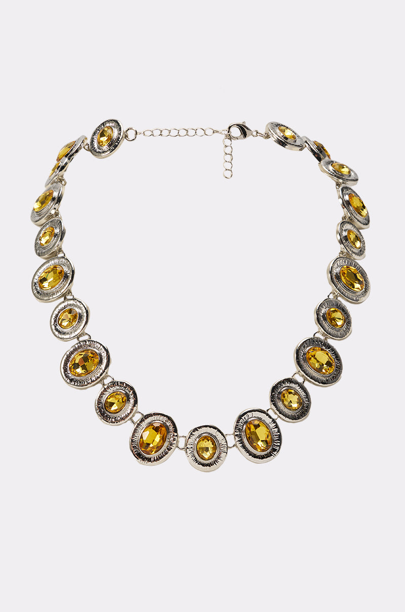The FEEL IT NECKLACE is a silver-tone statement piece with oval amber stones in decorative bezels, connected by a lobster clasp and adjustable chain, shown on a white background. 0