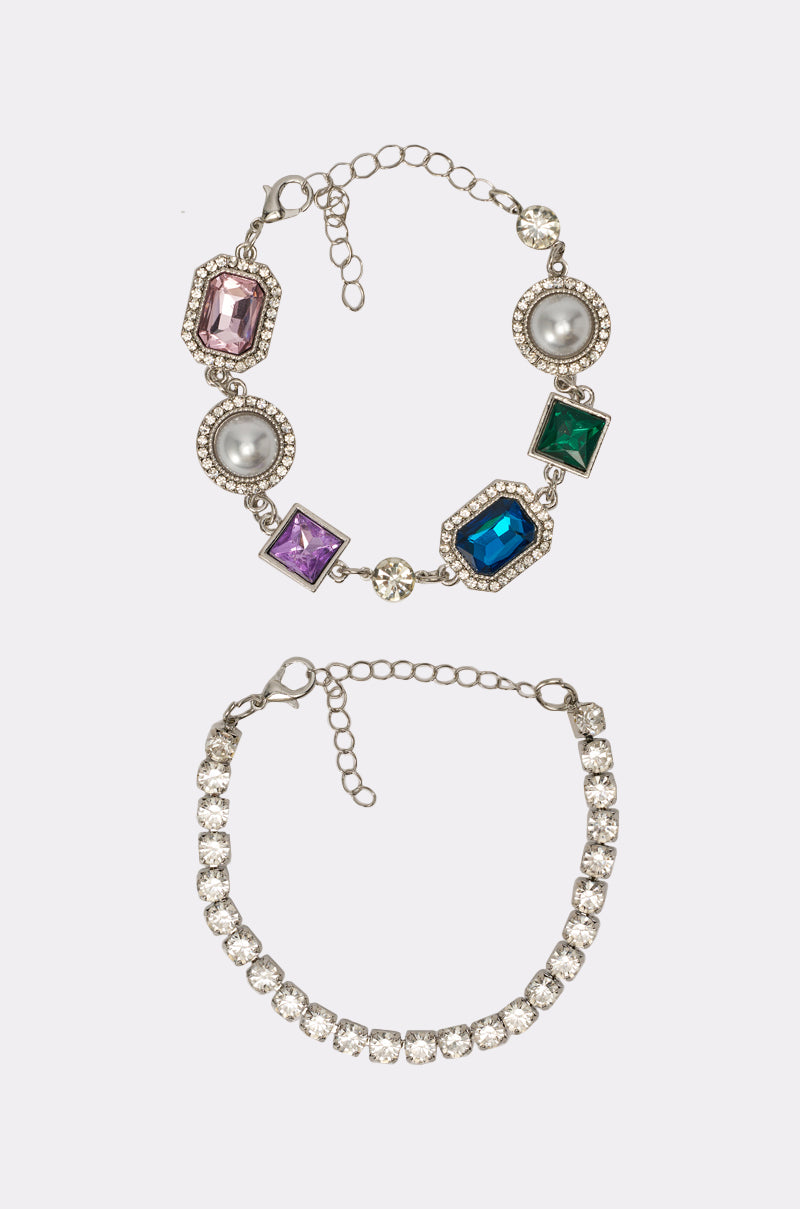 The QUEEN APPROVED BRACELET SET features two silver bracelets: a faux pearl bracelet with colorful gemstones and a simple rhinestone bracelet with clear crystals. Both have adjustable clasps and are shown on a white background. 1