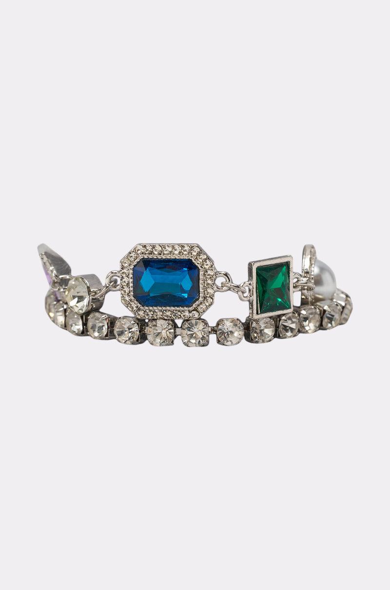 The QUEEN APPROVED BRACELET SET is a silver bracelet set with a large rectangular blue gemstone, a smaller square green gemstone, and clear rhinestones set in a decorative metal band. 2