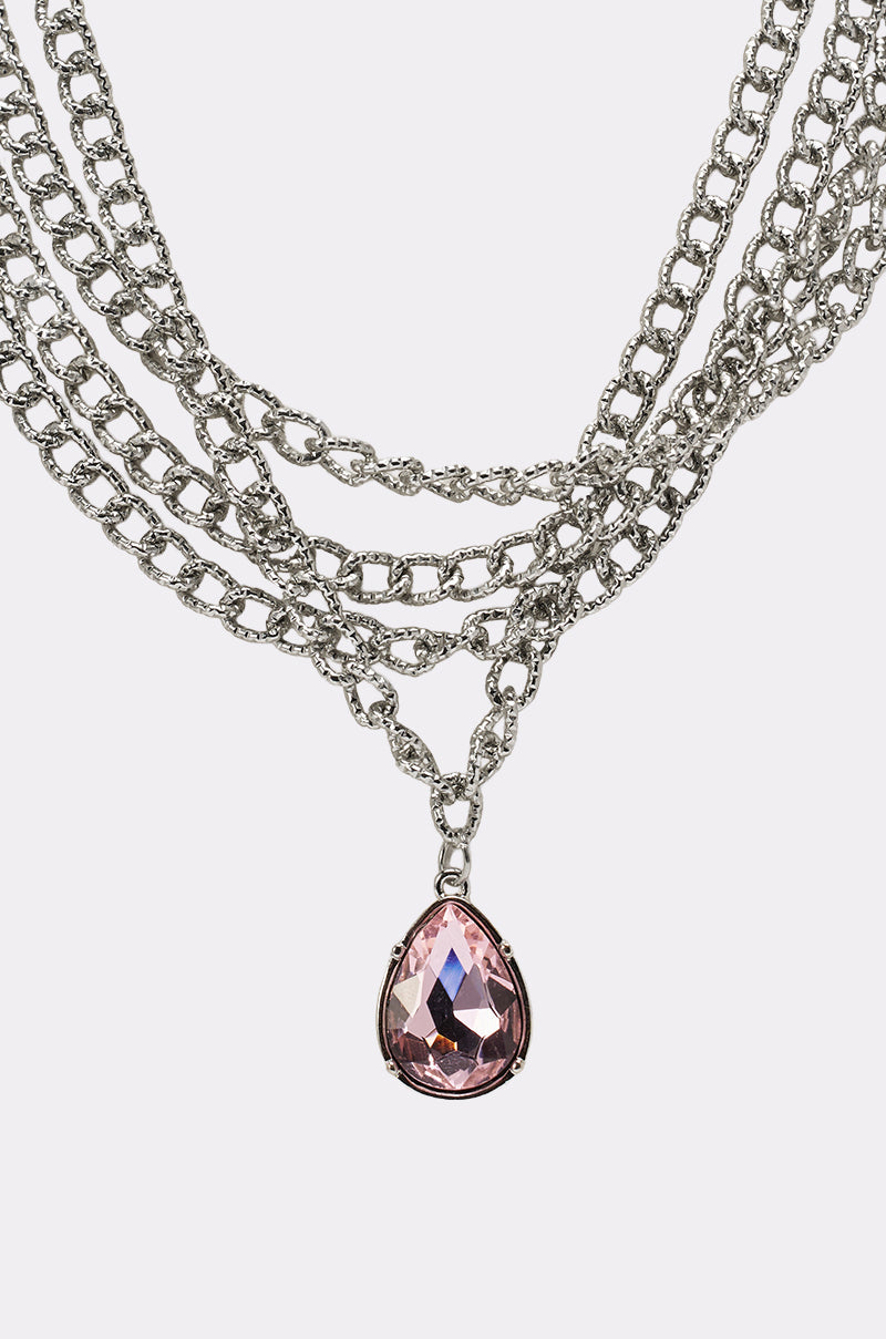 The PRINCESS TREATMENT NECKLACE is a beautiful layered chain necklace with a large, teardrop-shaped pink pendant showcased on a plain white background. 3