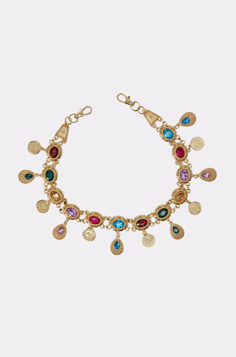The IM OUTSIDE PURSE CHAIN is a gold charm bracelet featuring colorful gemstones and detailed dangling gold coins, evoking the look of a jeweled purse chain, displayed on a white background. 1