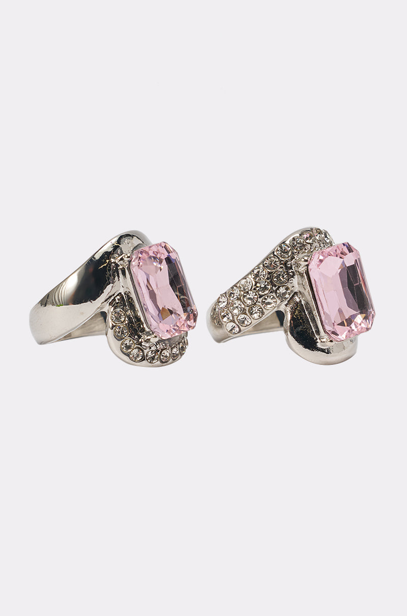 The PRETTY IN PINK RING SET features two chunky silver rings with large rectangular pink gemstones and small round clear crystals, displayed side by side on a white background. 2