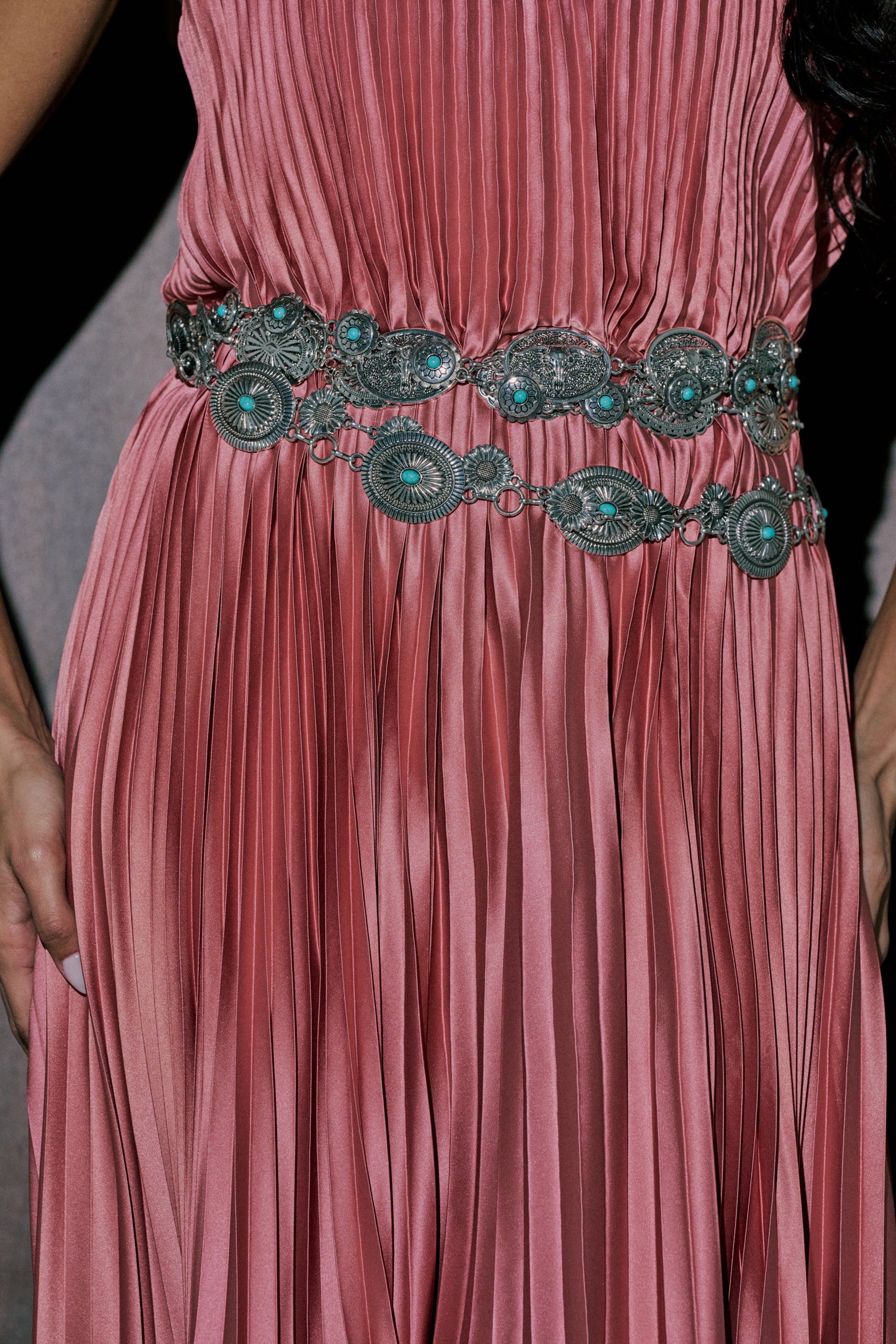 A person wearing a pleated rose-pink dress styled with the WILD WEST LAYERED CHAIN BELT, shown from shoulders to mid-thigh, hands at their sides. 1