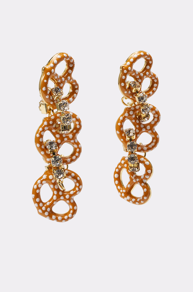 NEVER SALTY EARRING: Gold pretzel drop earrings with brown and white enamel accents, adorned with rows of sparkling clear stones. Shown on a plain white background. 2