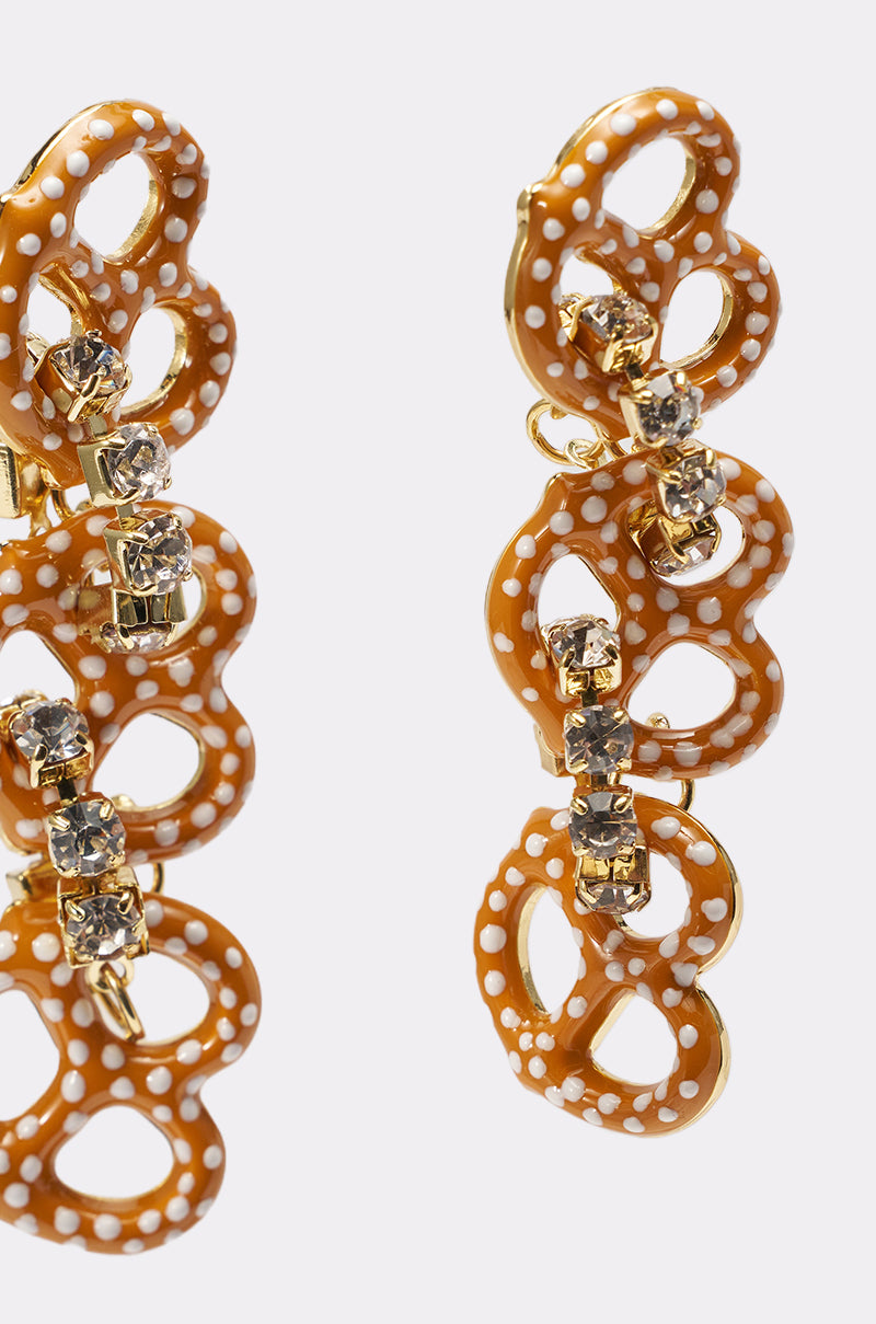 Close-up of NEVER SALTY EARRING—a pair of glossy pretzel-shaped drop earrings with white polka dots and sparkling rhinestone accents—set against a plain light background. 3