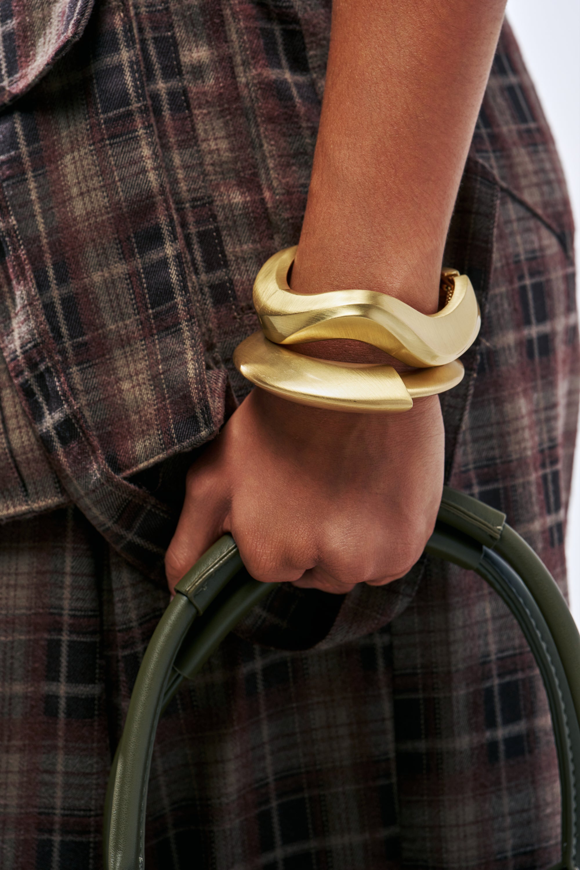A person wears two wide, wavy, gold ULTIMATE STACK BRACELET SET bangles on their wrist while holding a handbag.