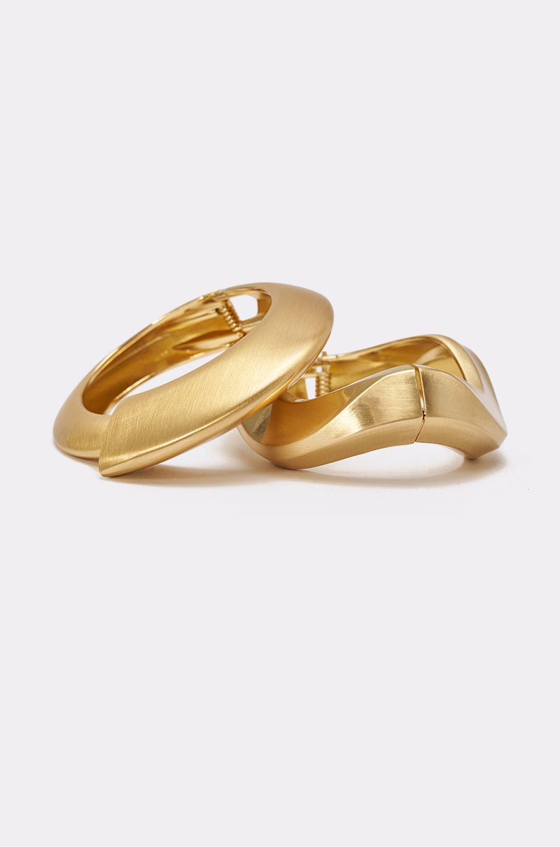 The ULTIMATE STACK BRACELET SET, featuring modern gold-toned bangles with a smooth matte finish, styled alongside other gold jewelry for a chic look—one lying flat and another slightly tilted on a plain white background. 2