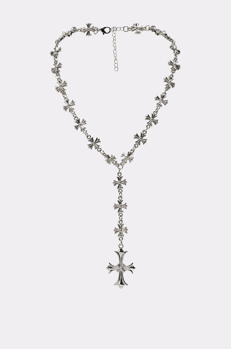 The CROSS YA LARIAT NECKLACE features silver-tone cross-shaped links and a bold ornate lariat pendant, showcased against a simple, light background. 0