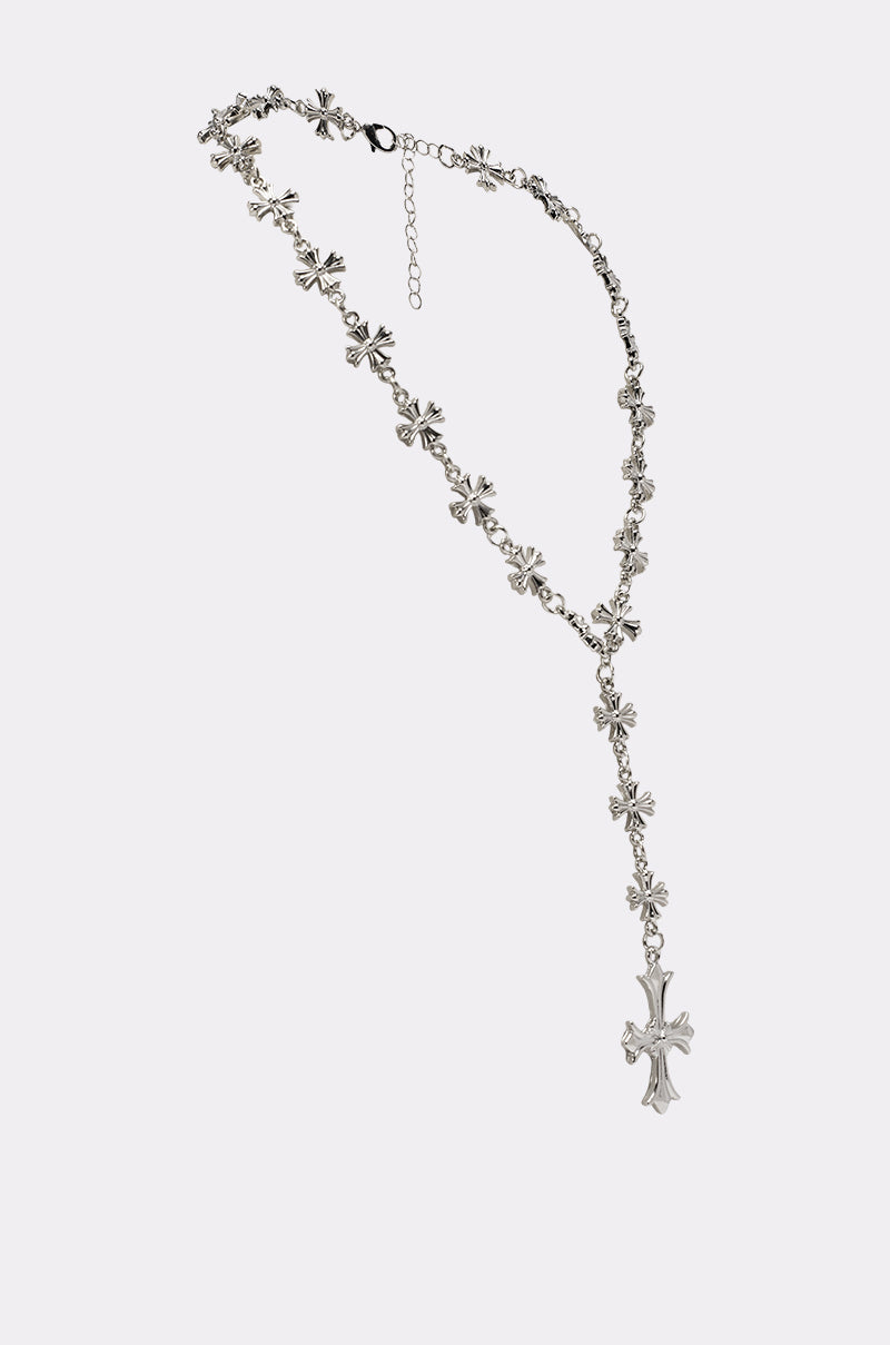 The CROSS YA LARIAT NECKLACE features multiple small silver-tone cross links and a larger cross pendant, inspired by rosary design, displayed on a plain light background. 2