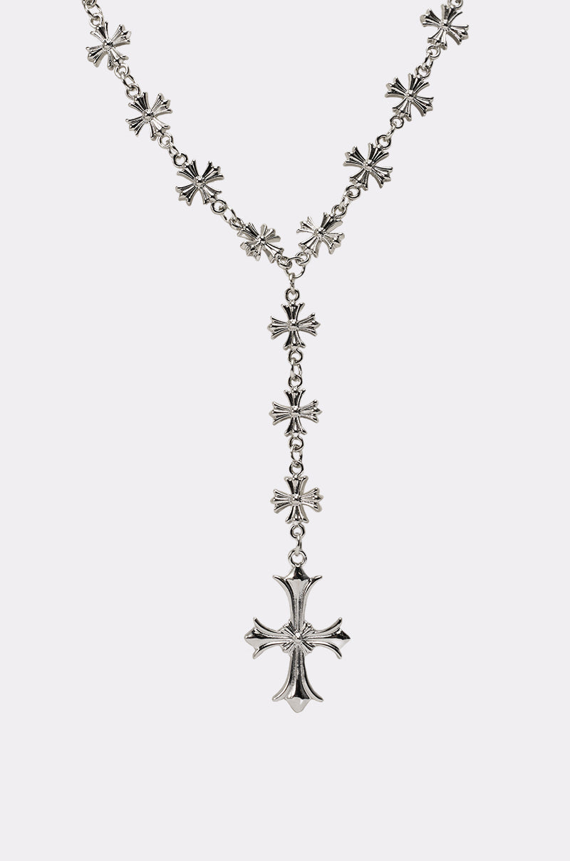 The CROSS YA LARIAT NECKLACE is a rosary-inspired silver-tone piece with small cross links and a bold, ornate central cross pendant, featuring an intricate symmetrical design displayed on a plain white background. 3