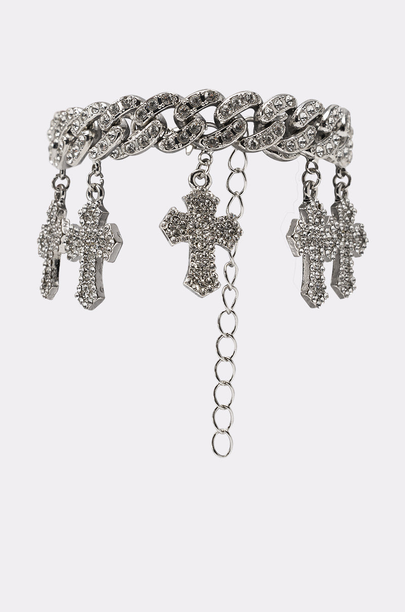 The ICED OUT CHARM BRACELET features a silver chunky curb-link design, sparkling rhinestones, and four dangling cross charms encrusted with rhinestones, shown against a light background. 0