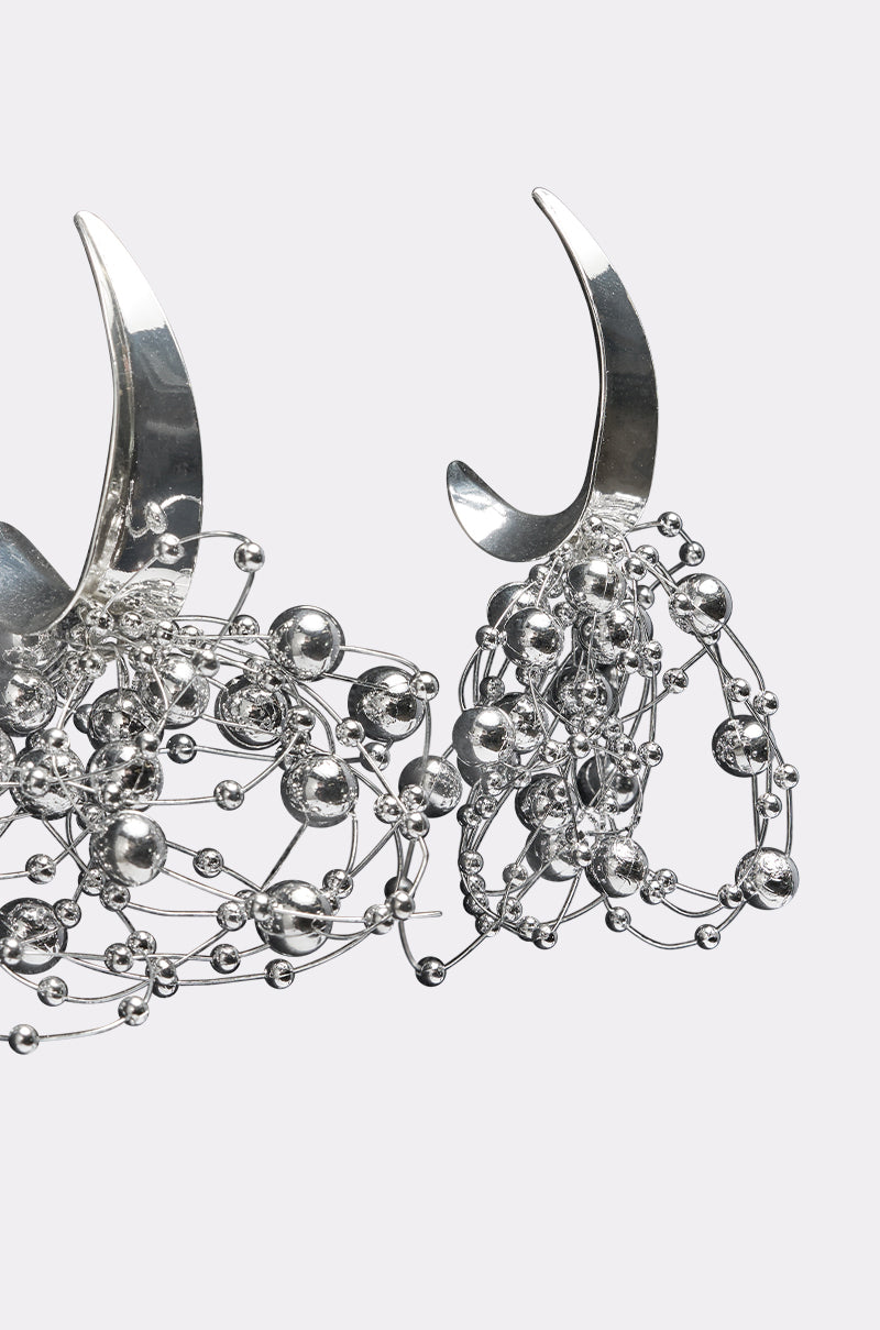 The BUBBLY EARRING features two metallic silver crescent shapes embellished with intricate wirework and small reflective beads, forming abstract silver-tone statement hoops shown against a plain white background. 3