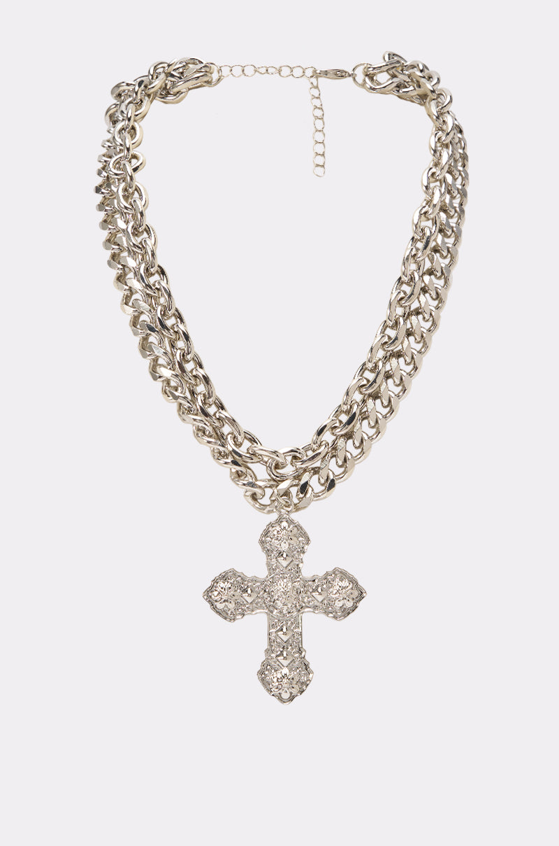 The HARDCORE SINNER NECKLACE is a bold, silver layered chain necklace featuring a large, ornate cross pendant encrusted with sparkling rhinestones. Displayed against a plain white background, this eye-catching piece is perfect for festival jewelry looks.