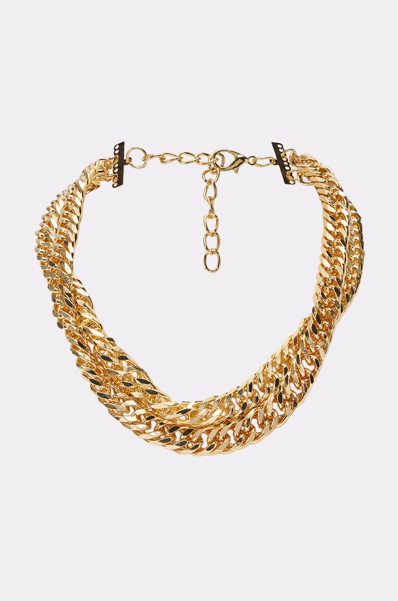 The FINE ME IN MIAMI DOUBLE CHAIN NECKLACE features gleaming intertwined gold curb links with an adjustable clasp and extension chain, making it a standout choice for maximalist jewelry lovers and creating a striking contrast against a plain white background.
