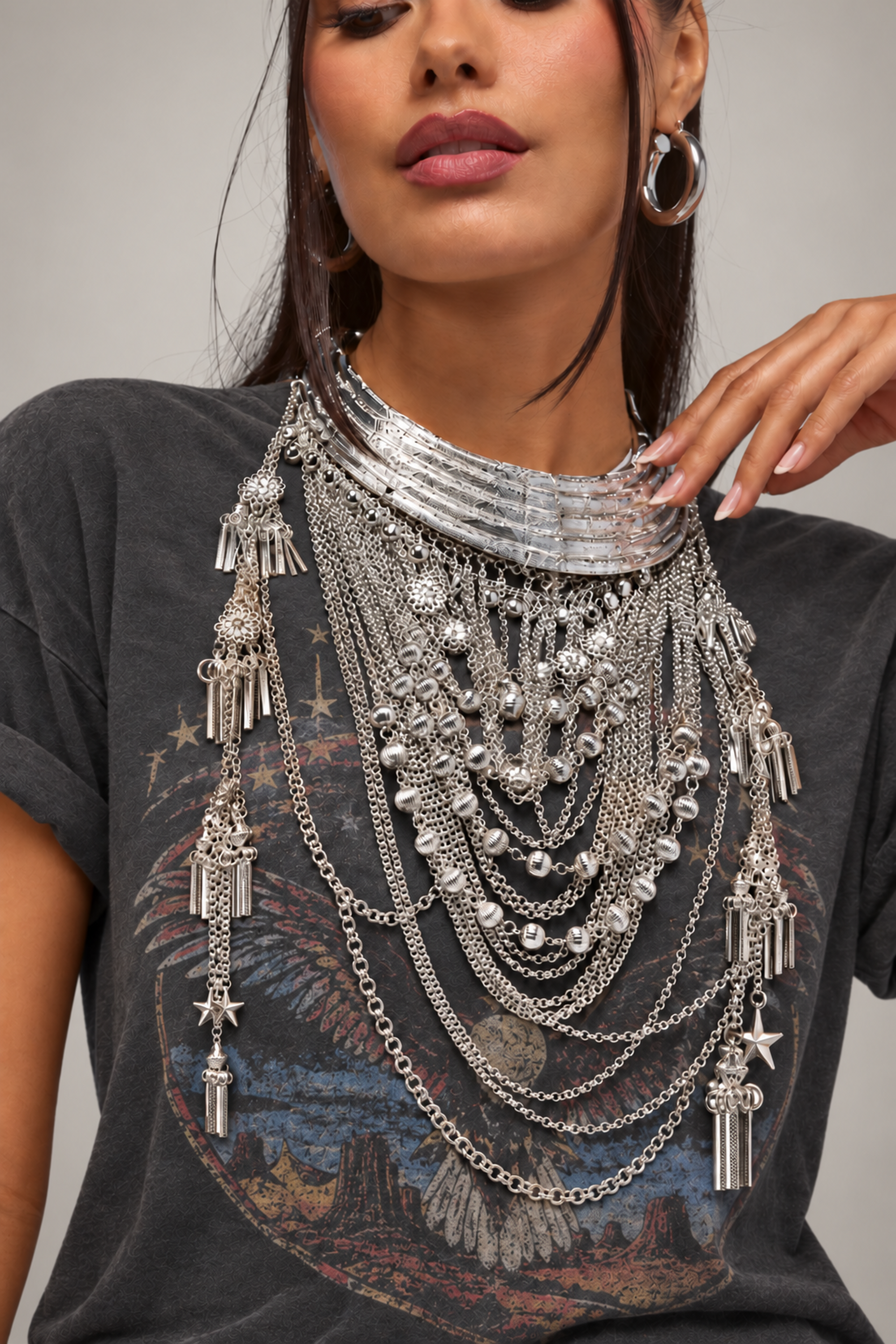 Wearing a dark graphic t-shirt, she styles her look with large hoop earrings and manicured nails, layering silver necklaces—including the REALLY RUN THIS STATEMENT NECKLACE featuring bold chains, pendants, beads, and Western-inspired engraved details.
