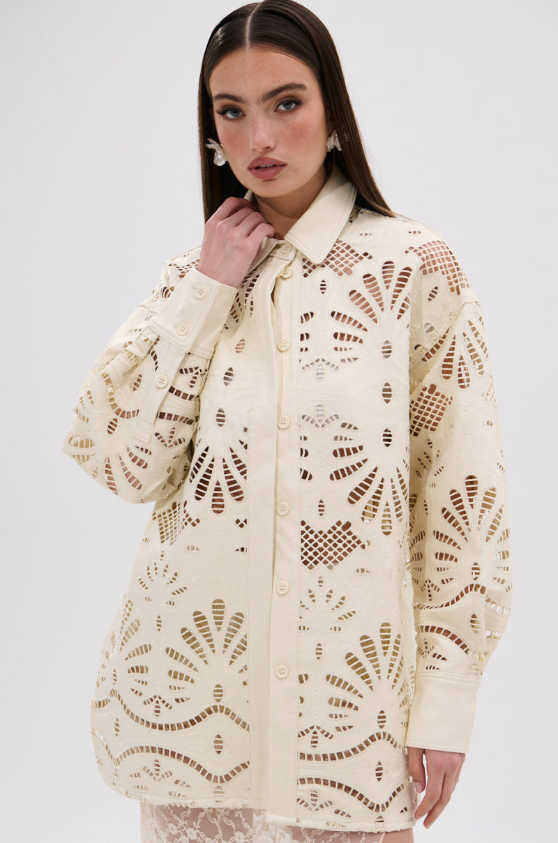 A woman with long brown hair models the YOU FEELIN ME NOW CUTOUT PU BUTTON UP SHIRT, a cream long-sleeve top with cutout details and a floral-inspired pattern, paired with a lace skirt against a plain white background.