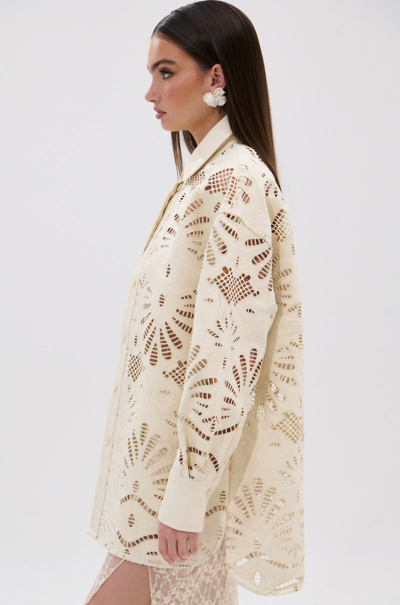A woman in profile wears the cream YOU FEELIN ME NOW CUTOUT PU BUTTON UP SHIRT with floral-inspired patterns and cutout details over a light lace skirt. She has long straight hair, flower earrings, and stands before a plain white background.