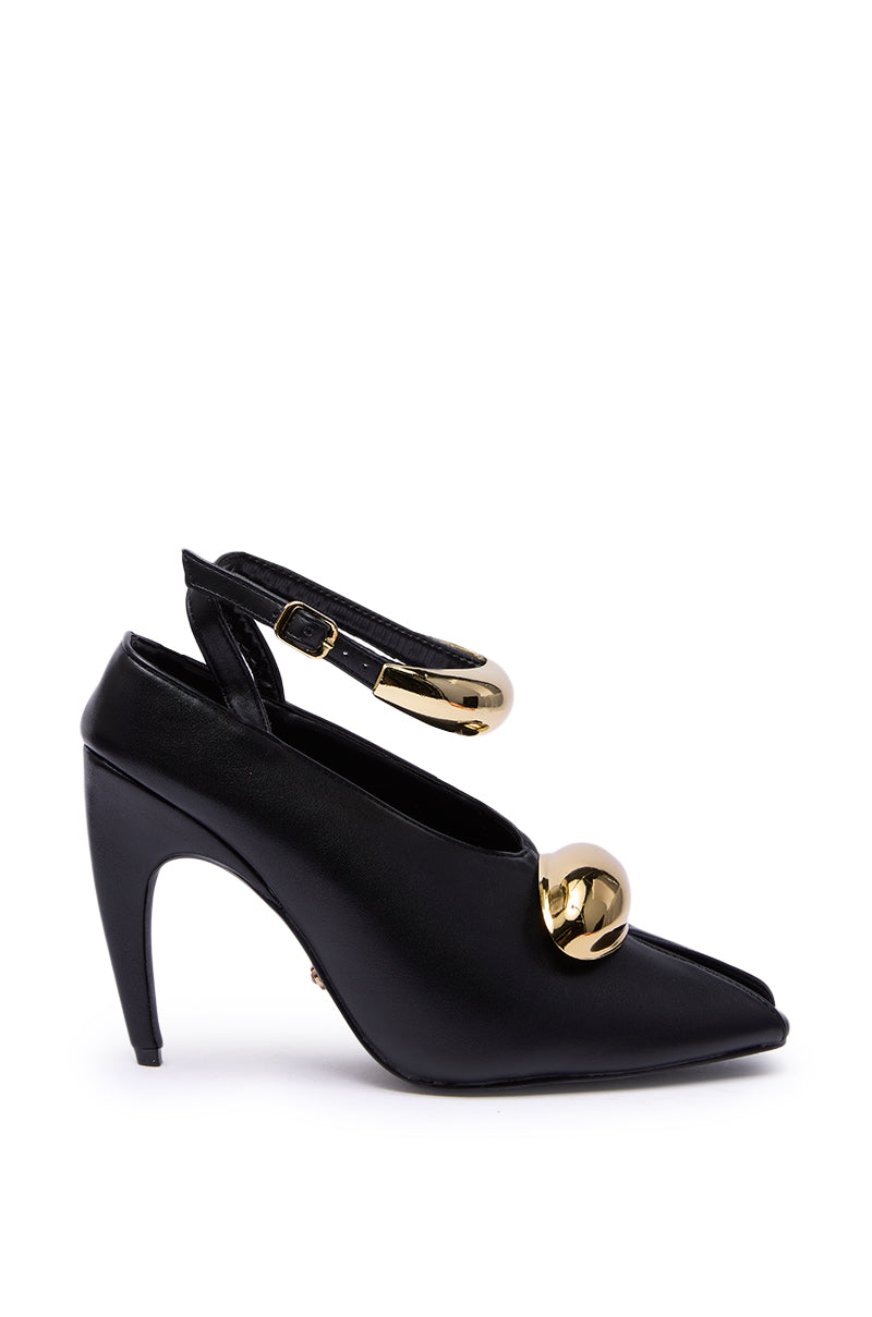 The AZALEA WANG HIMAH BLACK OPEN TOE PUMP features black faux leather, an ankle strap, and two large shiny gold spheres—one on the strap and one on the toe—all set against a white background.