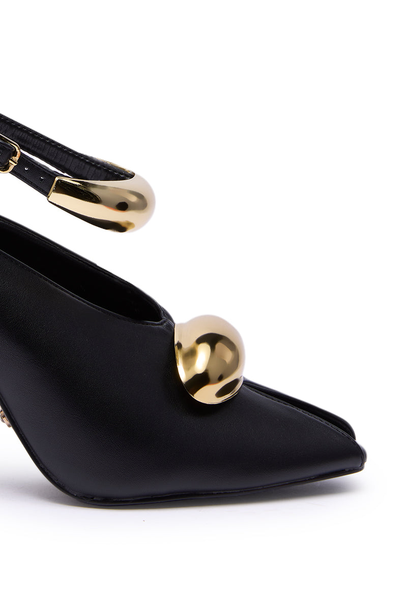 Close-up of the AZALEA WANG HIMAH BLACK OPEN TOE PUMP, a black faux leather high heel with open toe, adorned with a large shiny gold sphere and a matching gold ankle strap detail.