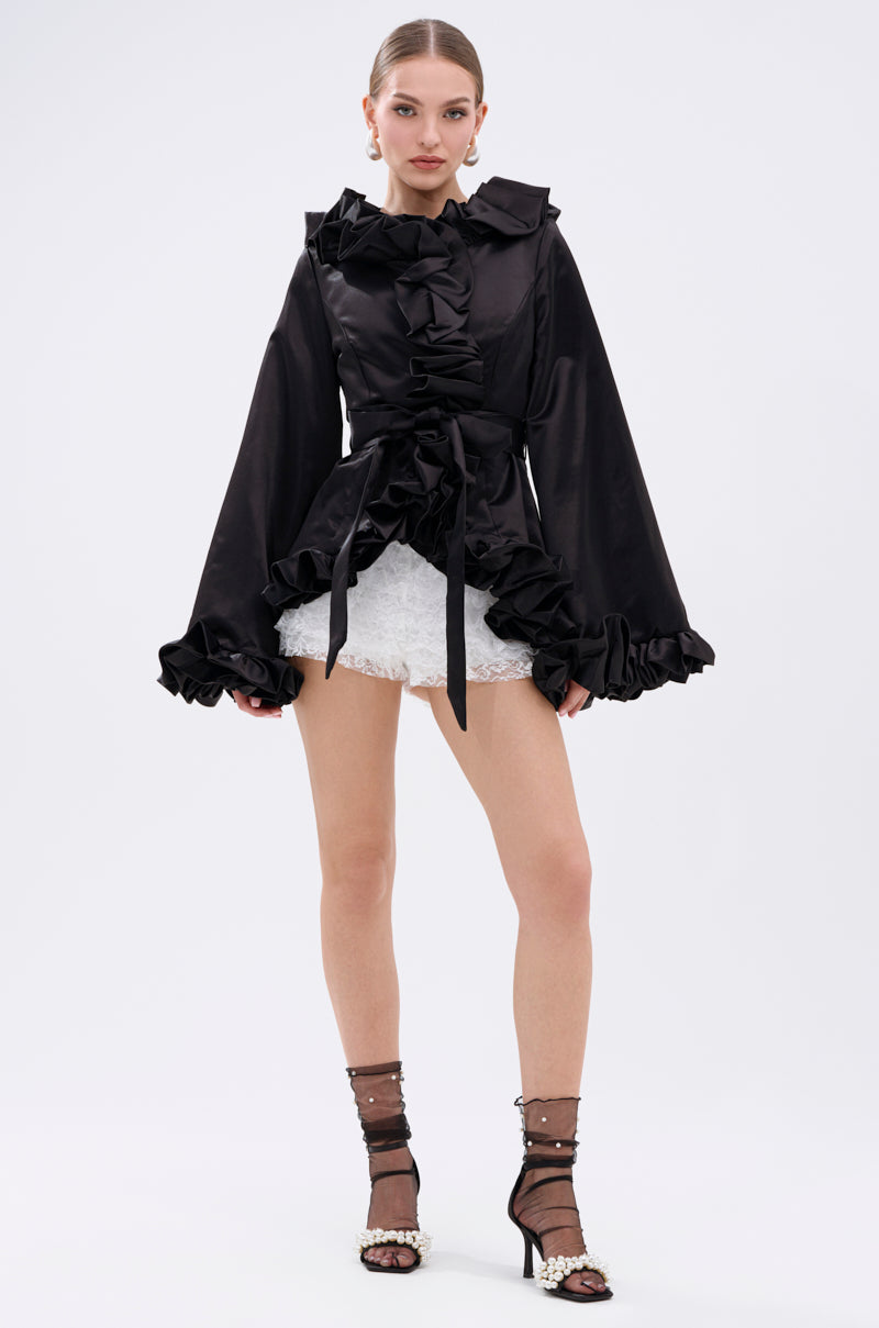 A woman faces forward wearing the GARDEN PARTY WRAP BLAZER in black with a bow tie at the waist, paired with white lace mini shorts, sheer black socks adorned with pearls, and open-toe heels against a plain light background. 8
