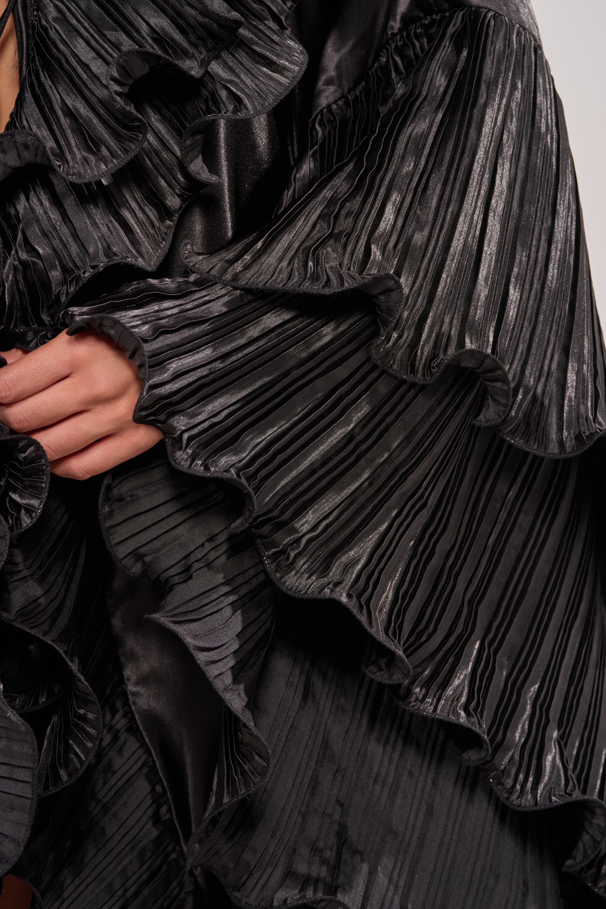 Close-up of a person’s hand resting on the SHINE ON LONG SLEEVE FRONT TIE TOP, highlighting its textured pleats and intricate, layered details in this striking statement blouse. 10