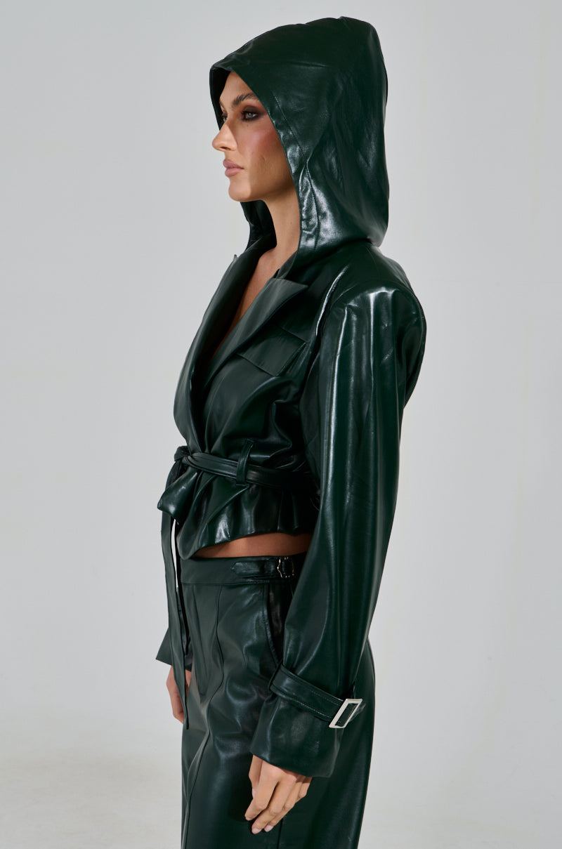 Clad in an evergreen MONTE CARLO HOODED MOTO faux leather jacket and matching skirt, a person looks sideways. The outfit features silver buckles and a belted waist against a light background.
