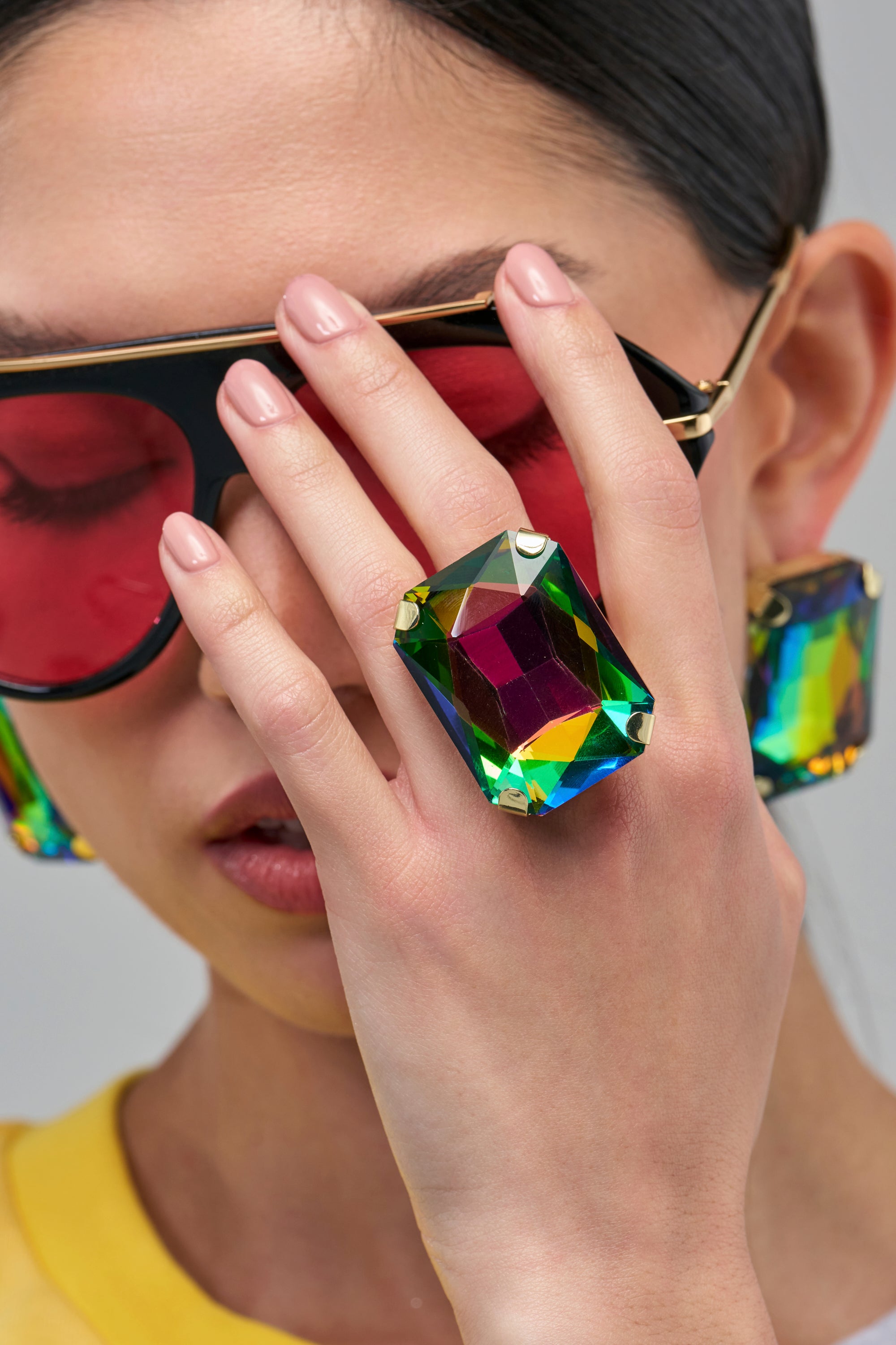 A person wearing the CYBER GLAM RING, an oversized, rectangular maximalist ring featuring a faceted, iridescent, multicolor gemstone.