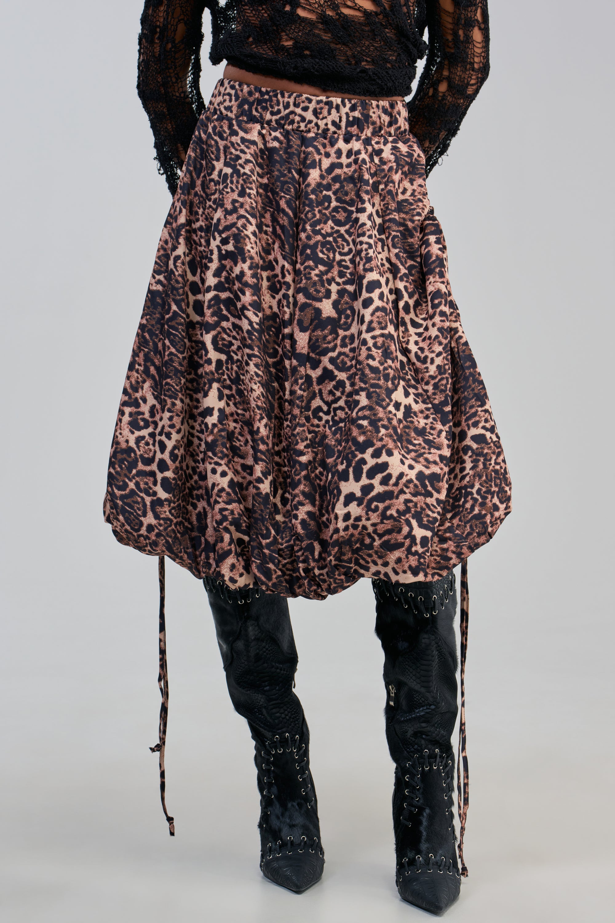 A person wearing a black lace top, the CHEETAH GIRL CHEETAH SISTER MIDI SKIRT—a voluminous cheetah print bubble skirt with adjustable tie details—and black pointed boots with studs, standing against a plain background.