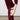 Dressed in a burgundy knit outfit, a person adjusts the AZALEA WANG HONOR WHITE SANDAL, made of fluffy cream-colored sherpa material, on their foot. This cozy open-toe sandal features three straps and is placed on a neutral floor against a plain white background.