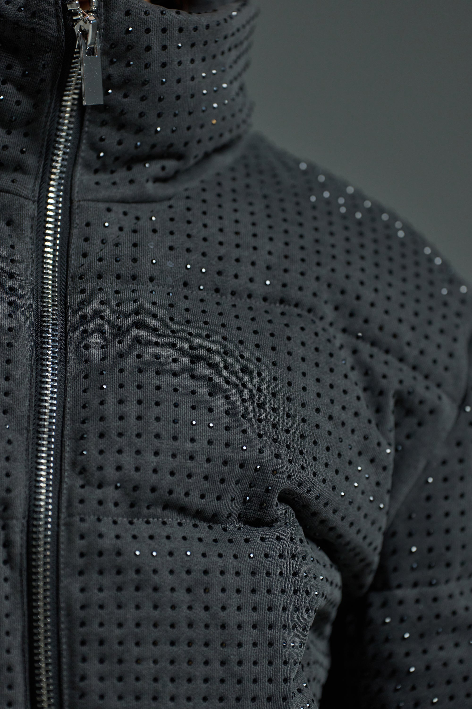 Close-up of the HOUDINI RHINESTONE PUFFER—black jacket featuring small, shiny rhinestones and a visible front zipper, set against a plain gray background.
