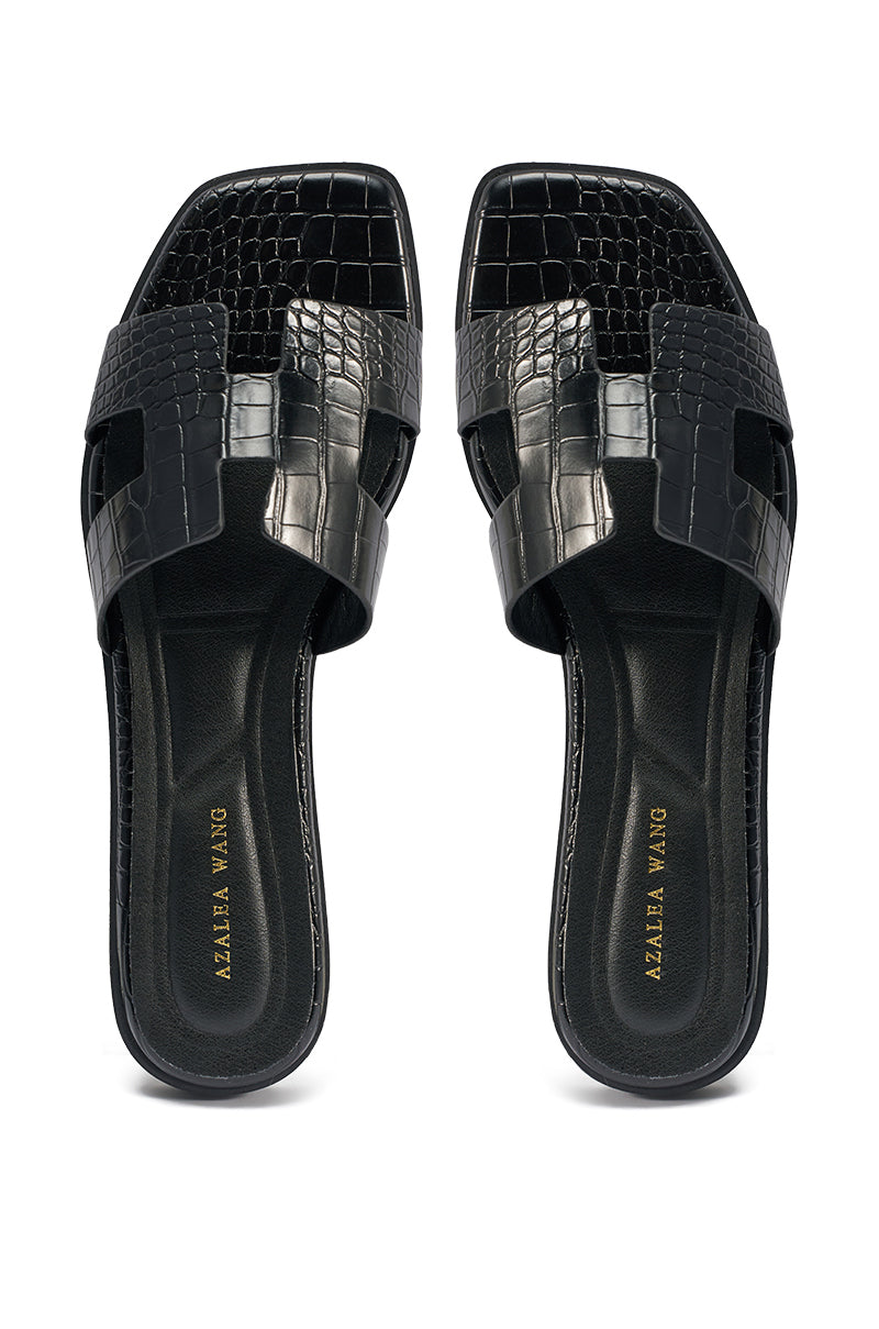 The AKIRA HOWDY BLACK CROC SLIP ON FLAT SANDAL is a black, crocodile-embossed faux leather slide with an open square toe, cut-out design, and gold "AZALEA WANG" branding on the insole. 3