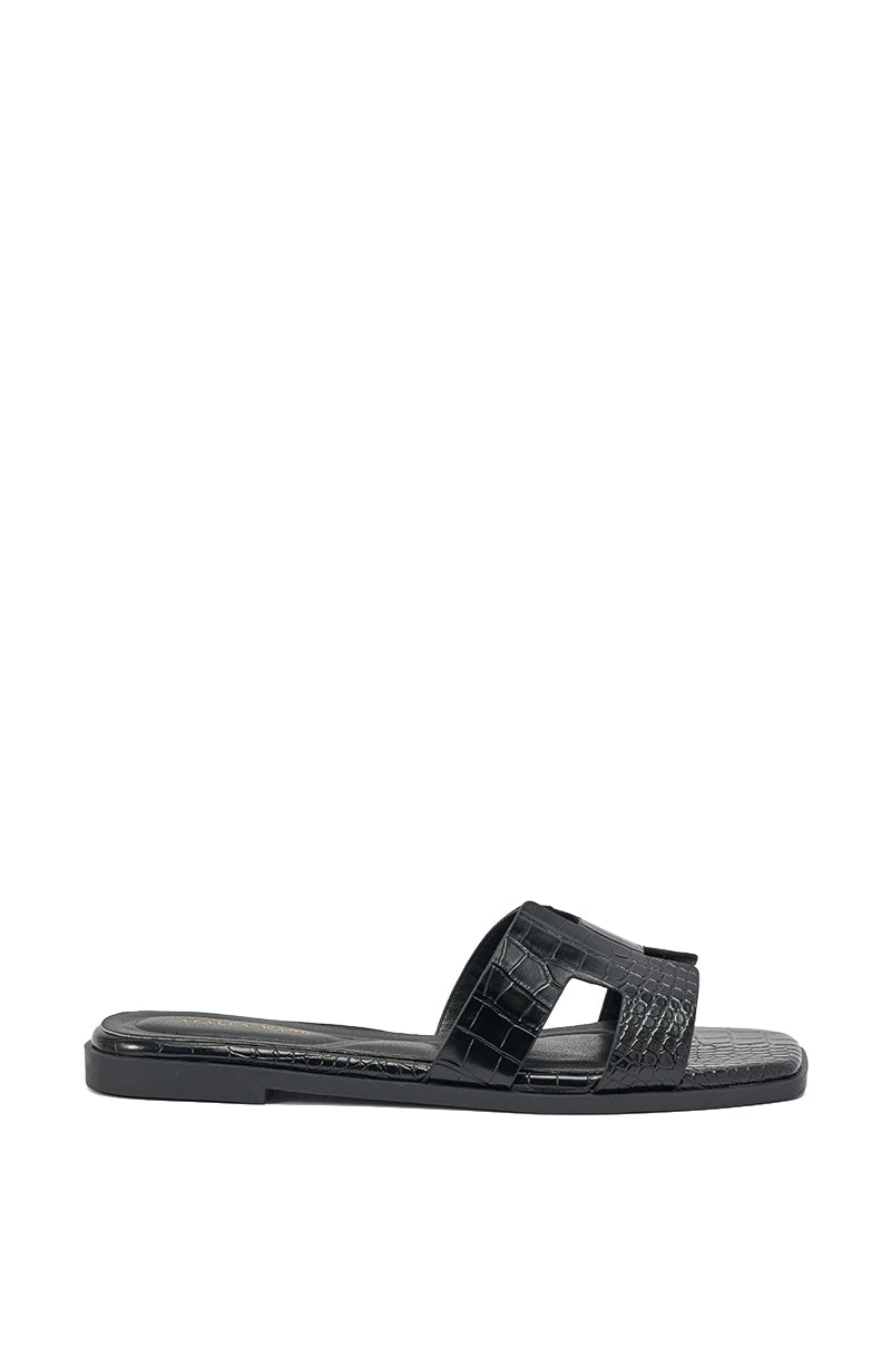 The AKIRA HOWDY BLACK CROC SLIP ON FLAT SANDAL features crocodile-embossed faux leather with a textured cutout strap, shown in side profile against a white background. 4