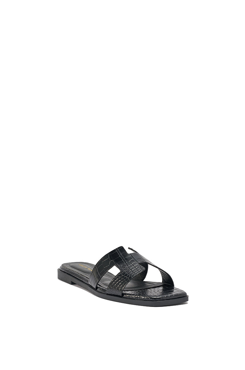 The AKIRA HOWDY BLACK CROC SLIP ON FLAT SANDAL features a flat sole and wide, crisscrossed crocodile-embossed faux leather straps, with a textured finish, angled slightly right on a plain white background. 5