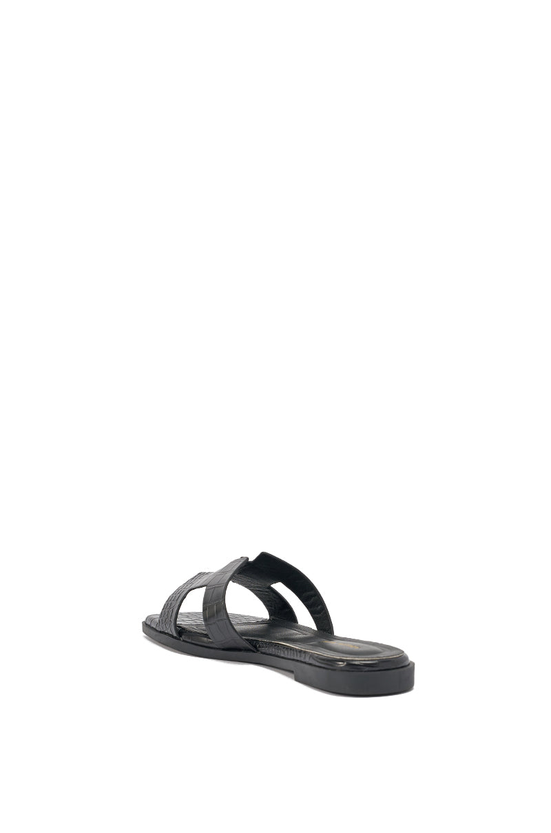 The AKIRA HOWDY BLACK CROC SLIP ON FLAT SANDAL features a black, crocodile-embossed faux leather woven crisscross strap, shown from the back right on a white background. 6