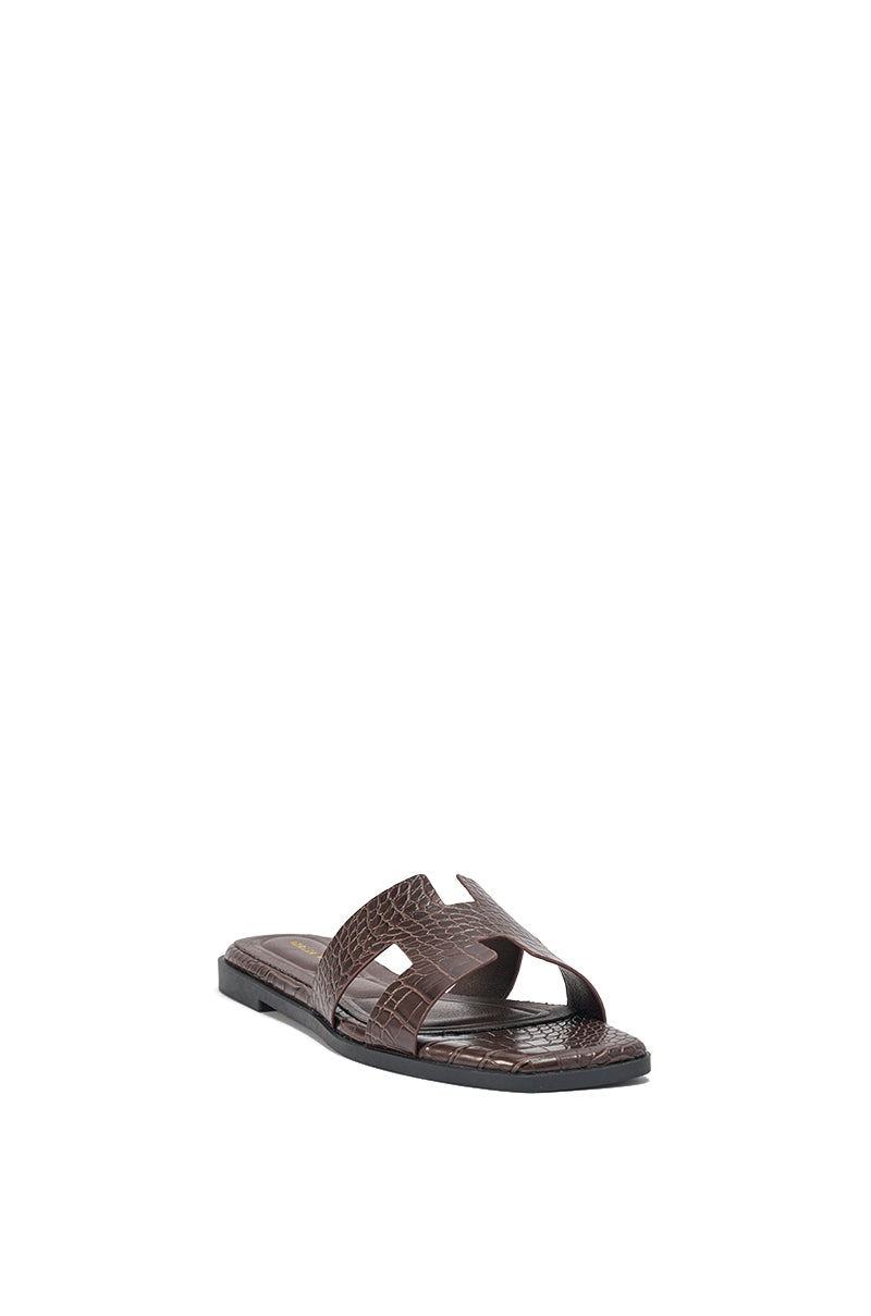 The AKIRA HOWDY BROWN CROC SLIP ON FLAT SANDAL is a brown slide with crocodile-embossed faux leather, a textured finish, and an open square toe, displayed against a plain white background. 7