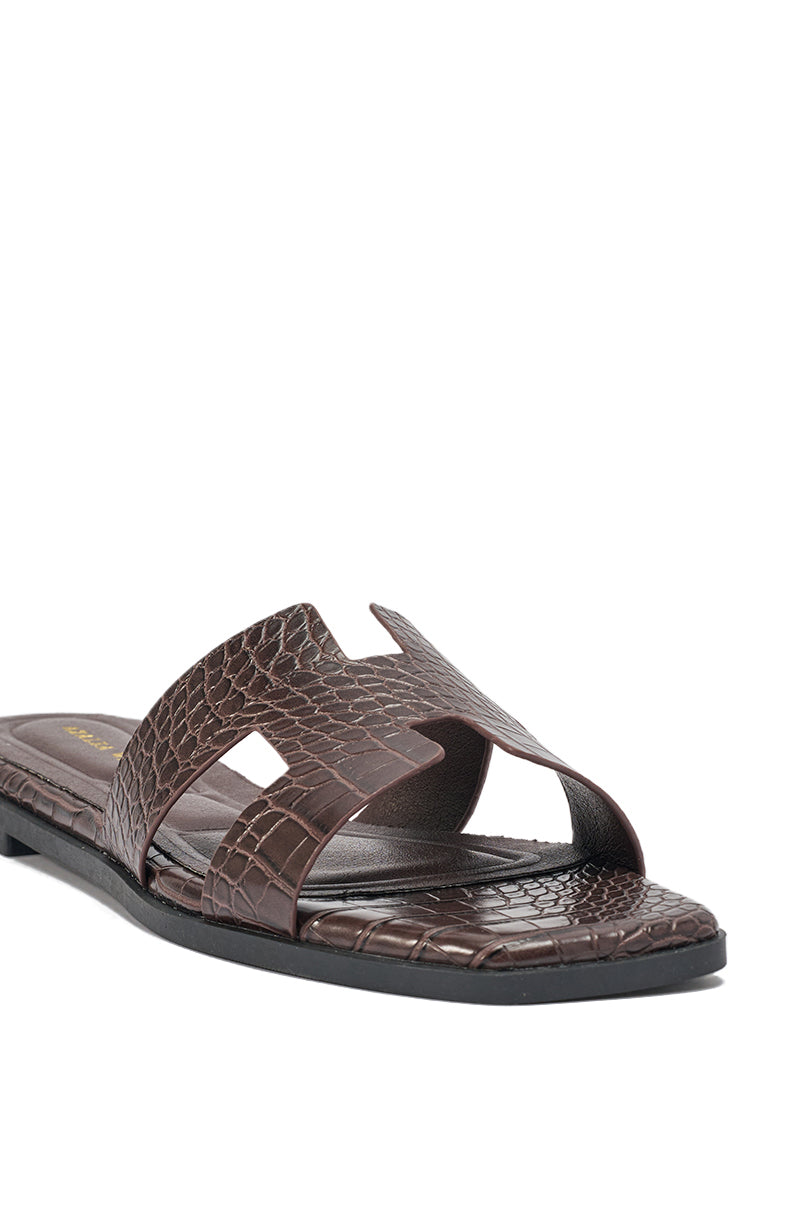 The AKIRA HOWDY BROWN CROC SLIP ON FLAT SANDAL features a brown, crocodile-embossed faux leather square toe, open toe design, and a cutout wide strap, shown against a white background. 9