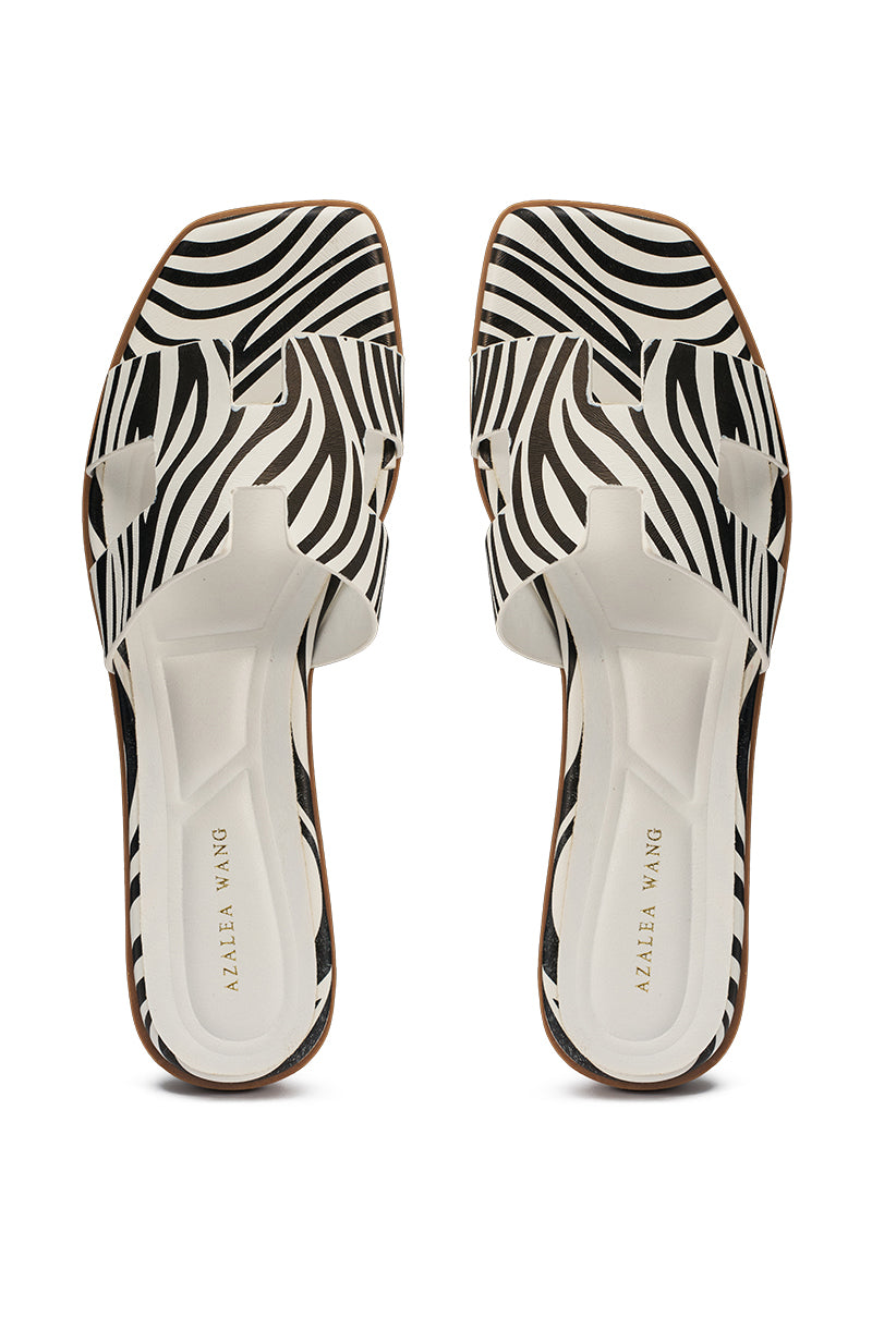 The AKIRA HOWDY ZEBRA SLIP ON FLAT SANDAL features black and white zebra stripes, open toes, cut-out strap details, and a comfort cushion insole with "ALAAIA WANG" on white insoles. 3